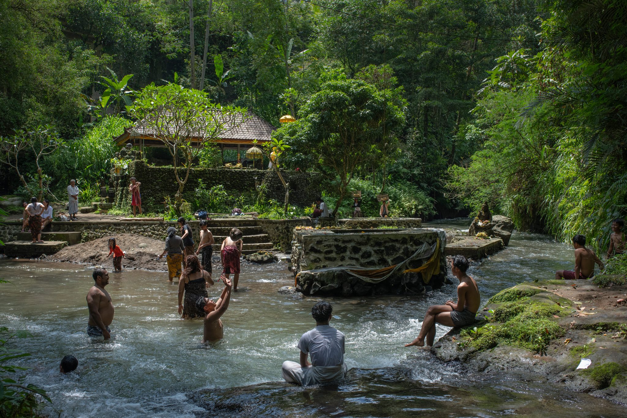 Dozens of bathers fill the river beneath the temple and its thatched pavilion.