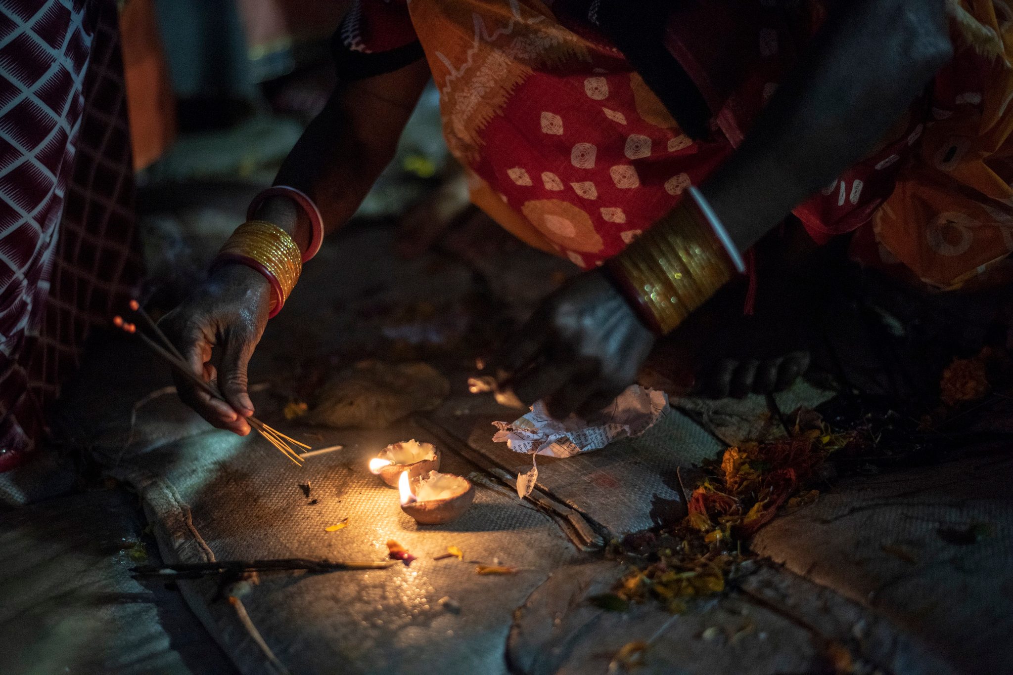 Bangled hands light a small flame and a stick of incense on the riverbank.