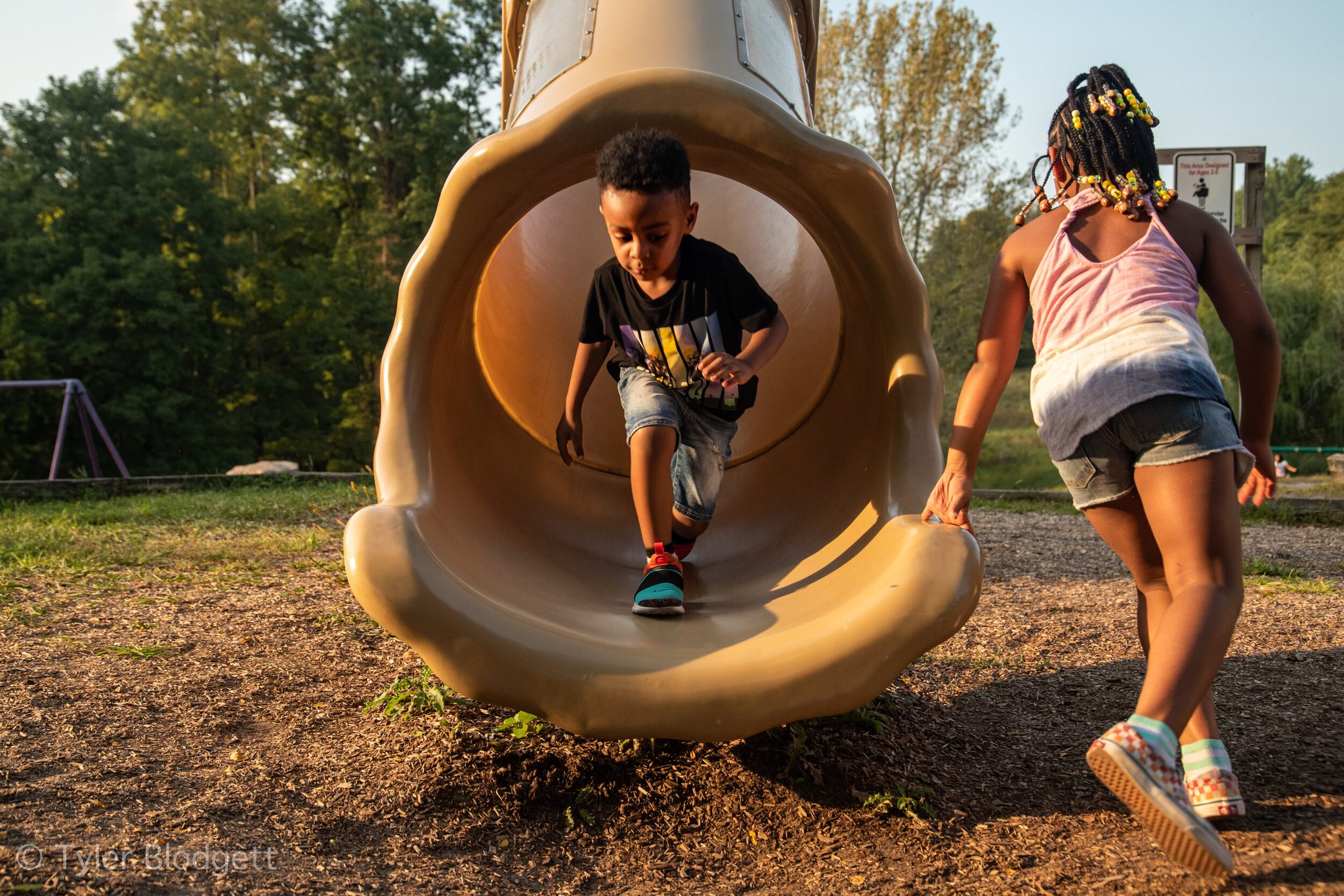 A boy shoots out of the tube slide while his friend races around for another turn.