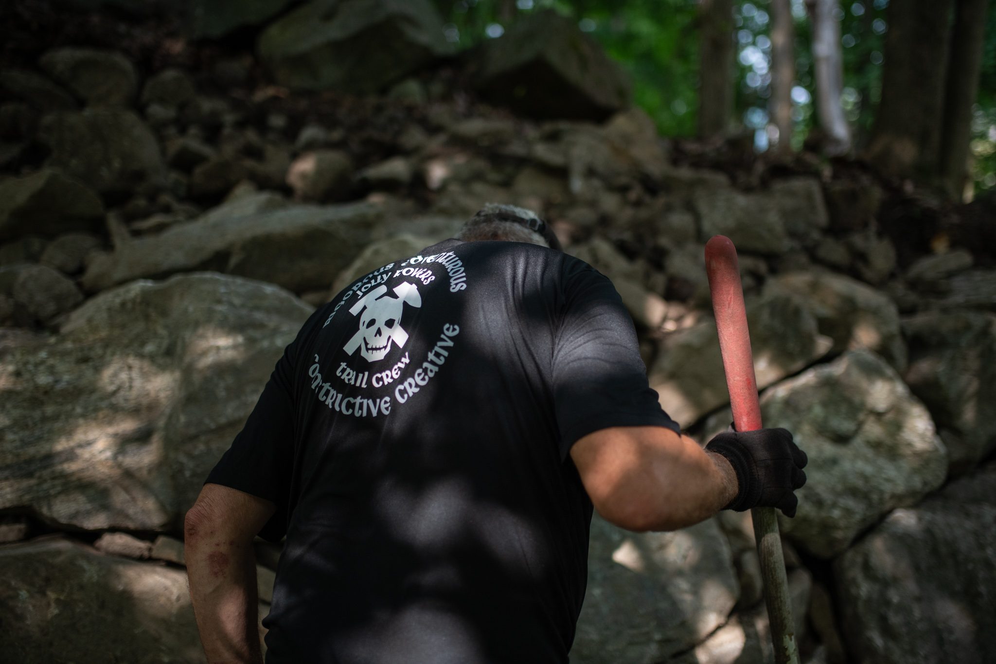 Seen from behind, he levers a stone loose with a pry bar.