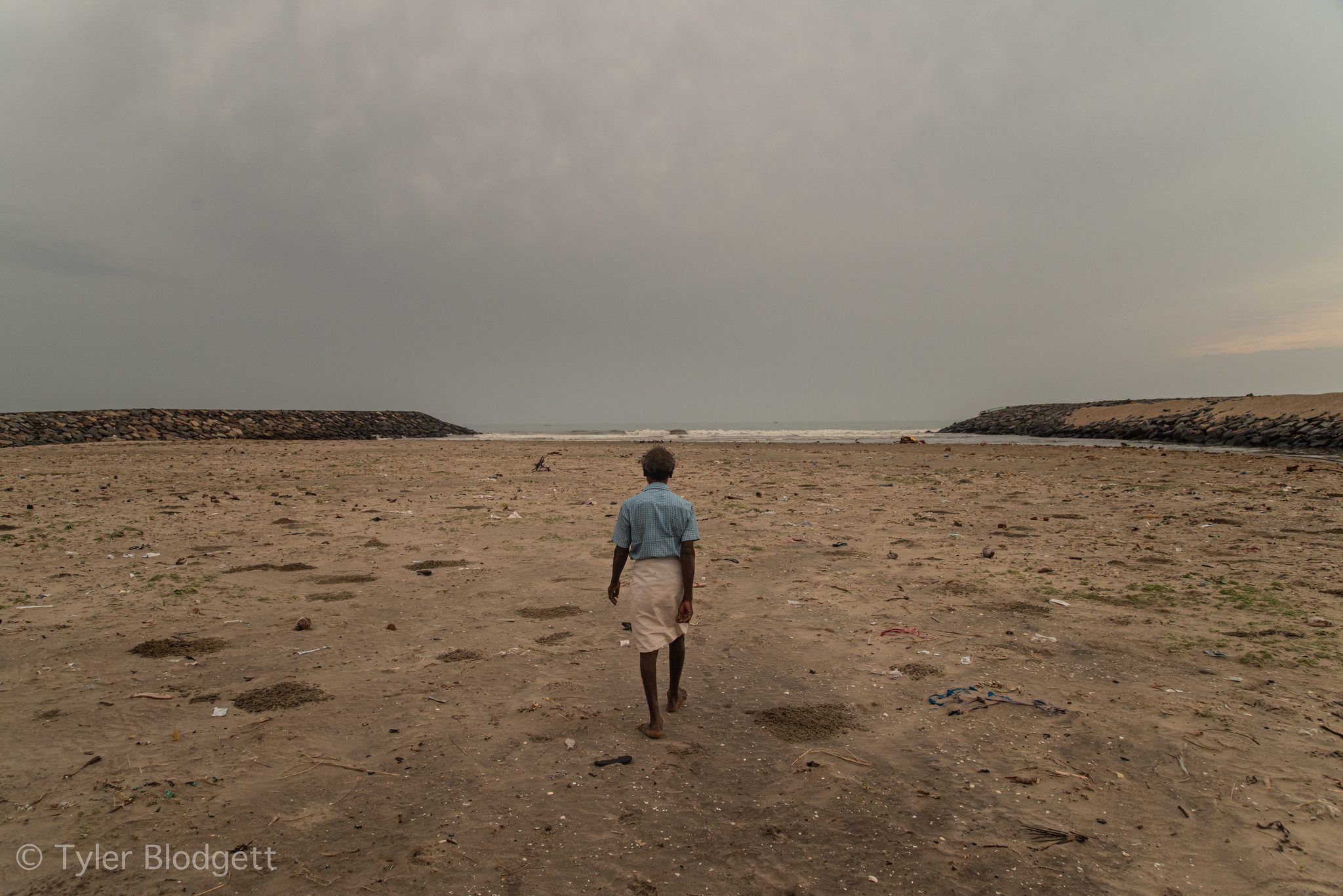 A man walks toward the sea between the breakwaters at the river's mouth.