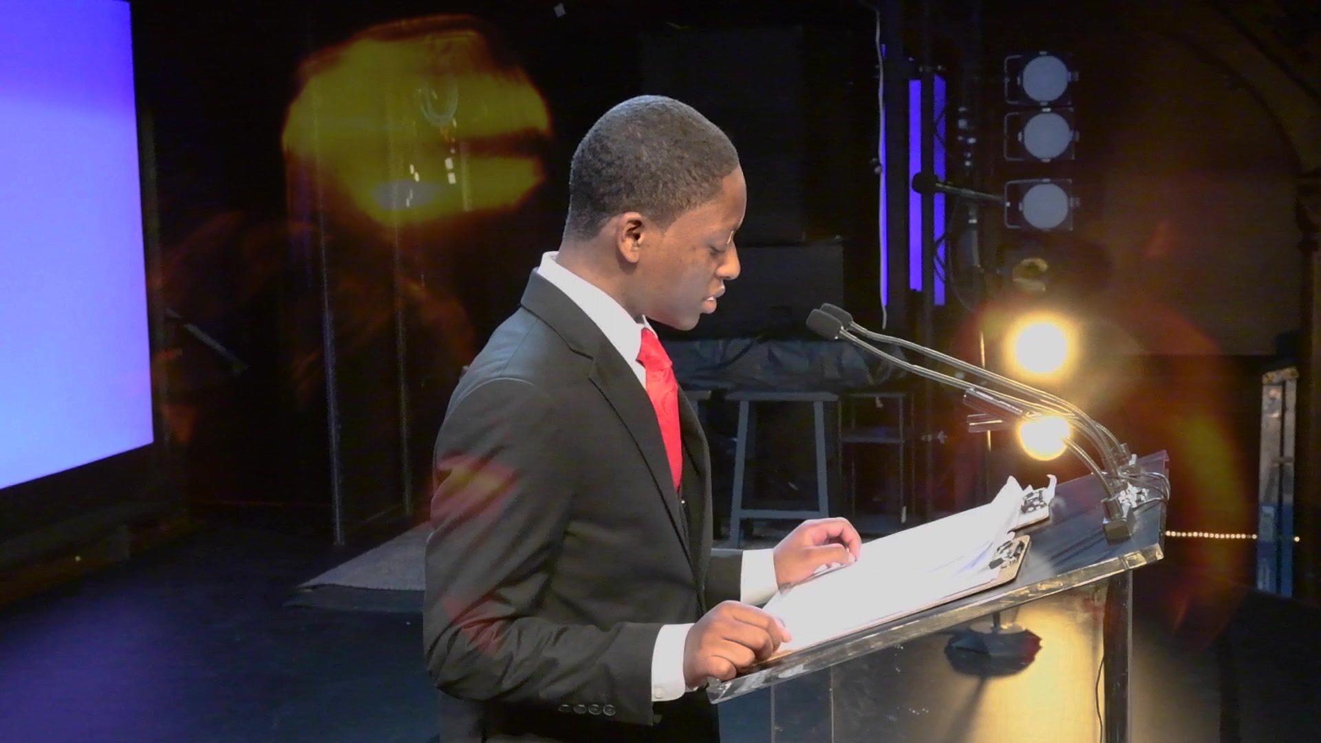 A graduate reads his speech at the podium, red tie and pocket square.