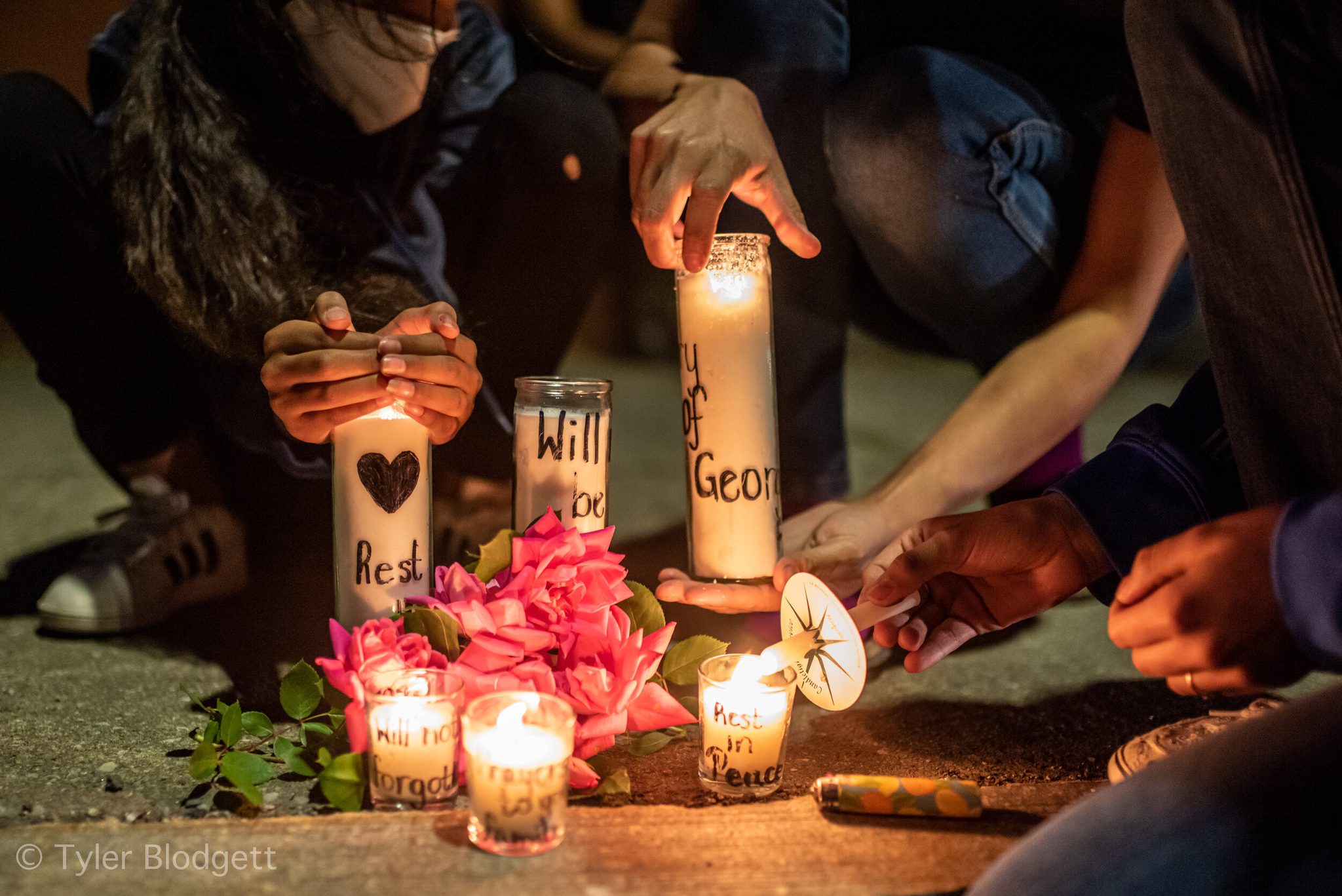 Handwritten candles for George Floyd gather with pink flowers on the pavement.