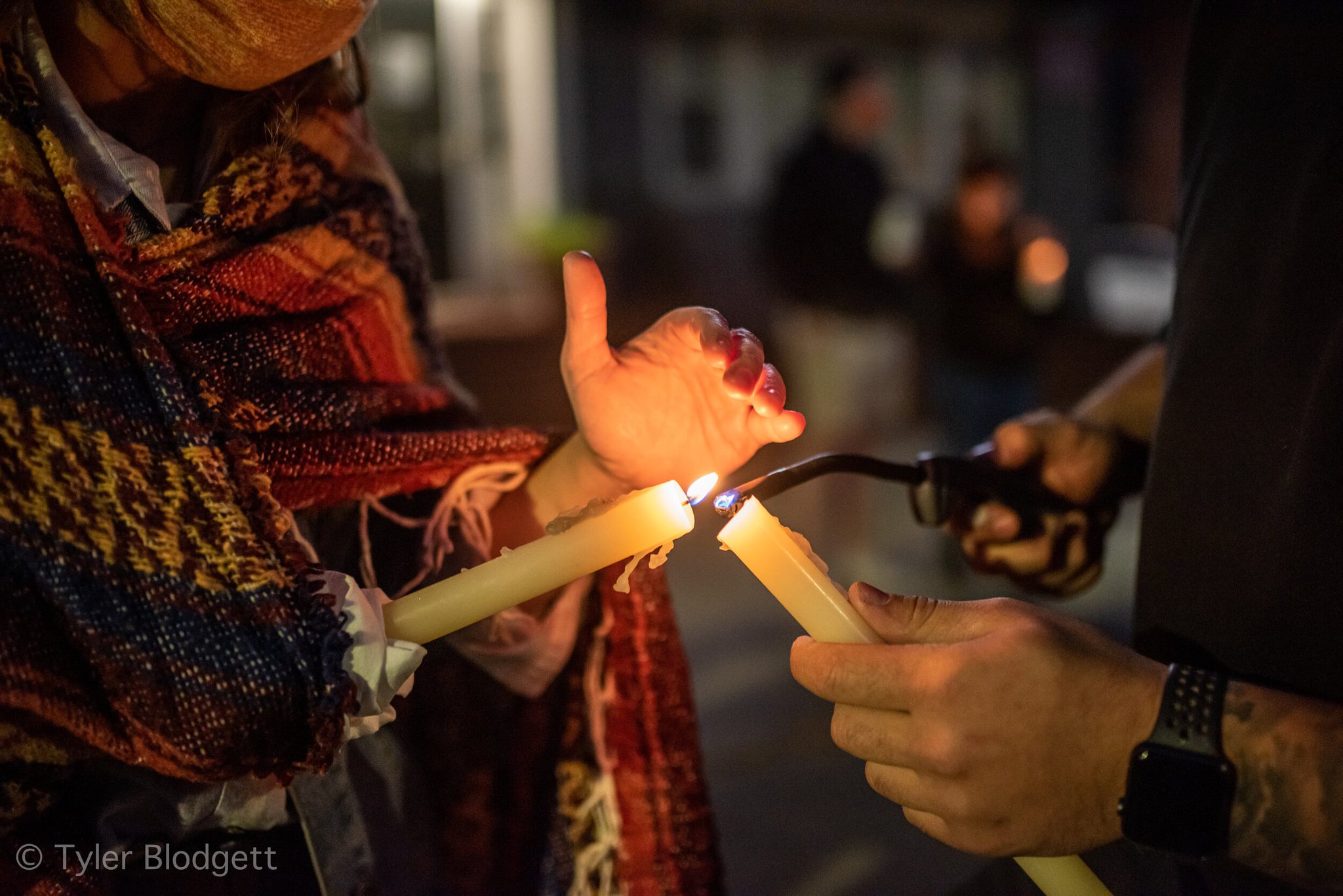 Hands pass the flame from candle to candle as night falls.