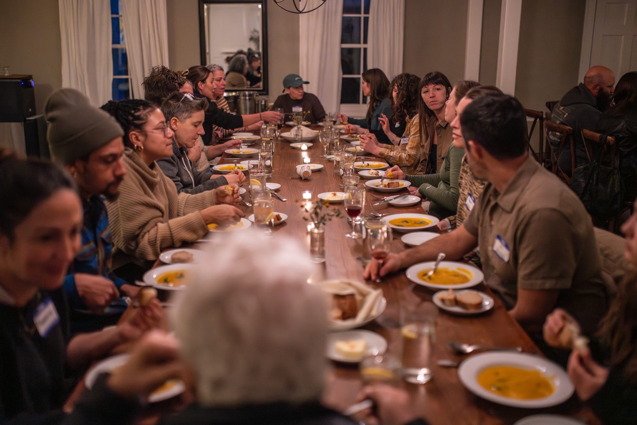 Soup and candlelight down one long table at dinner.