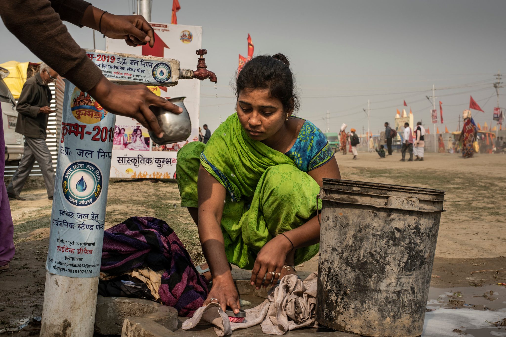 Woman cleans clothes at the roadside faucet.