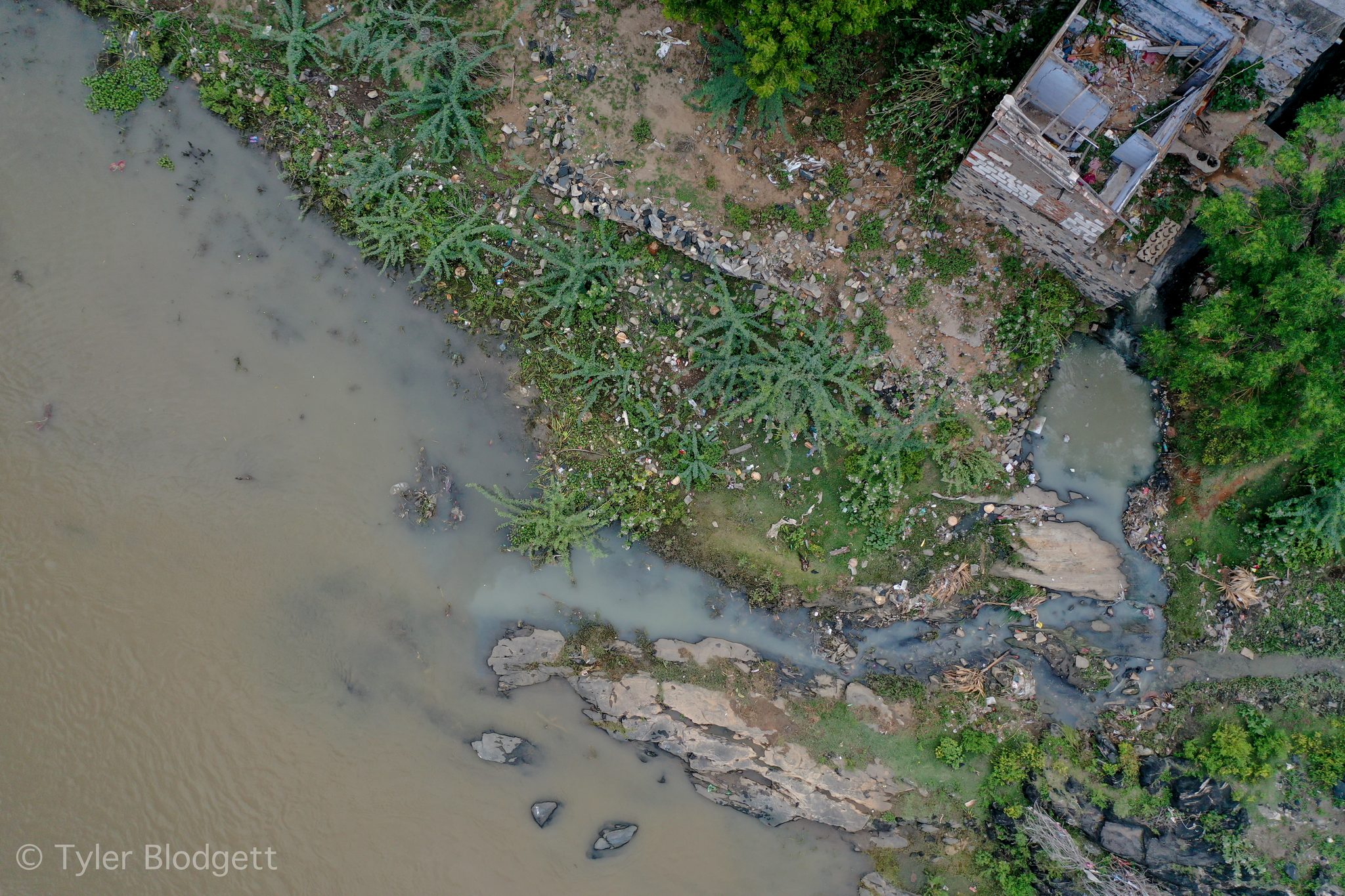 Straight down, a drain spills into the river beside a crumbling house.