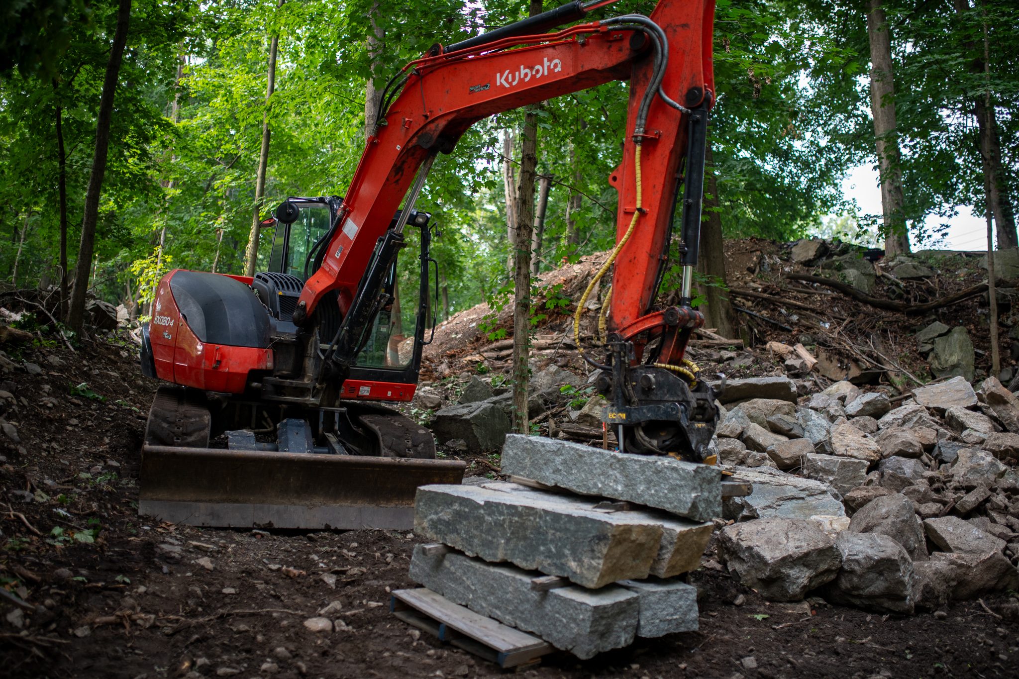 The excavator stretches its arm over a pile of rubble and a fresh row of granite.