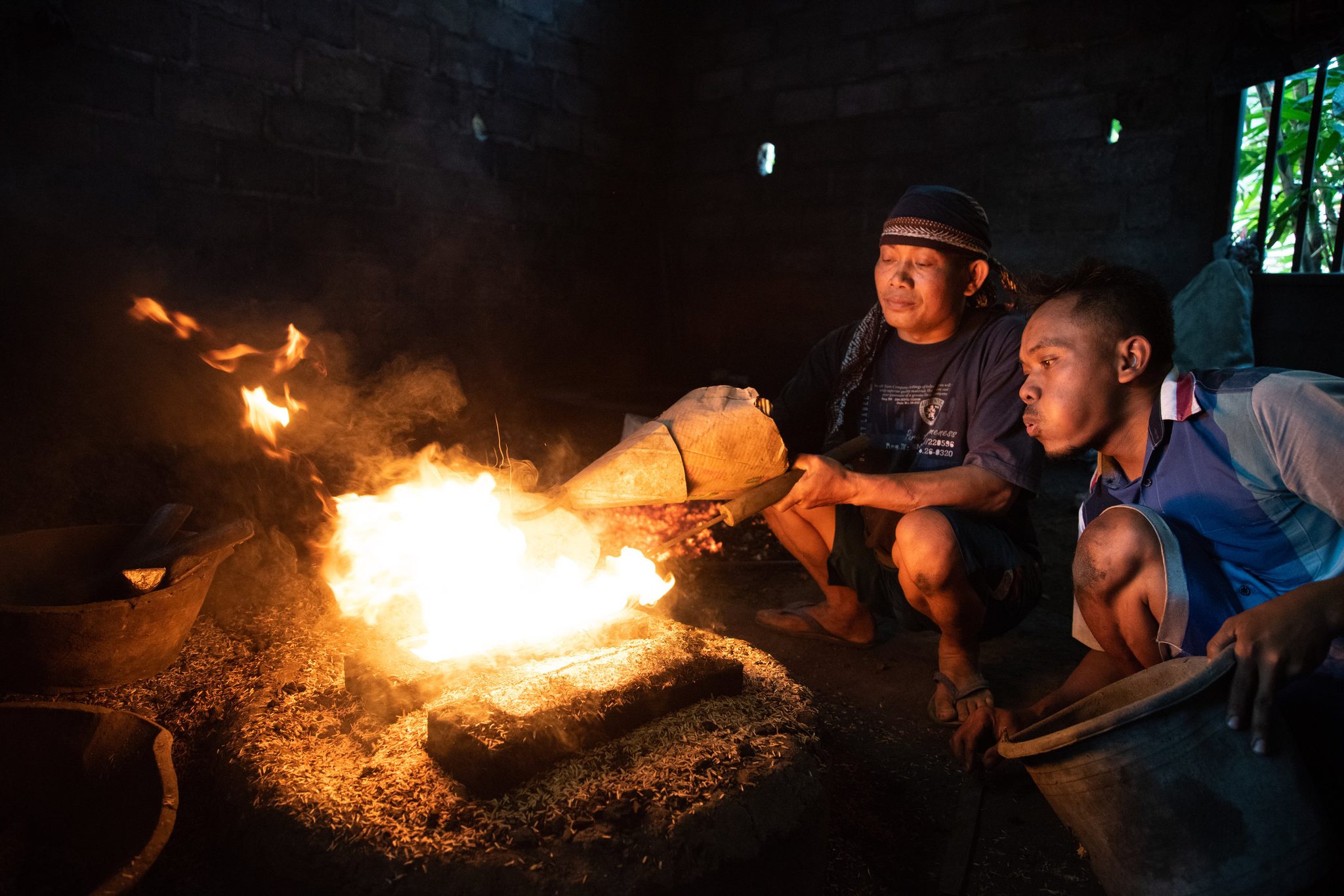 Two workers lean in as the molten metal meets the mold in a burst of flame.