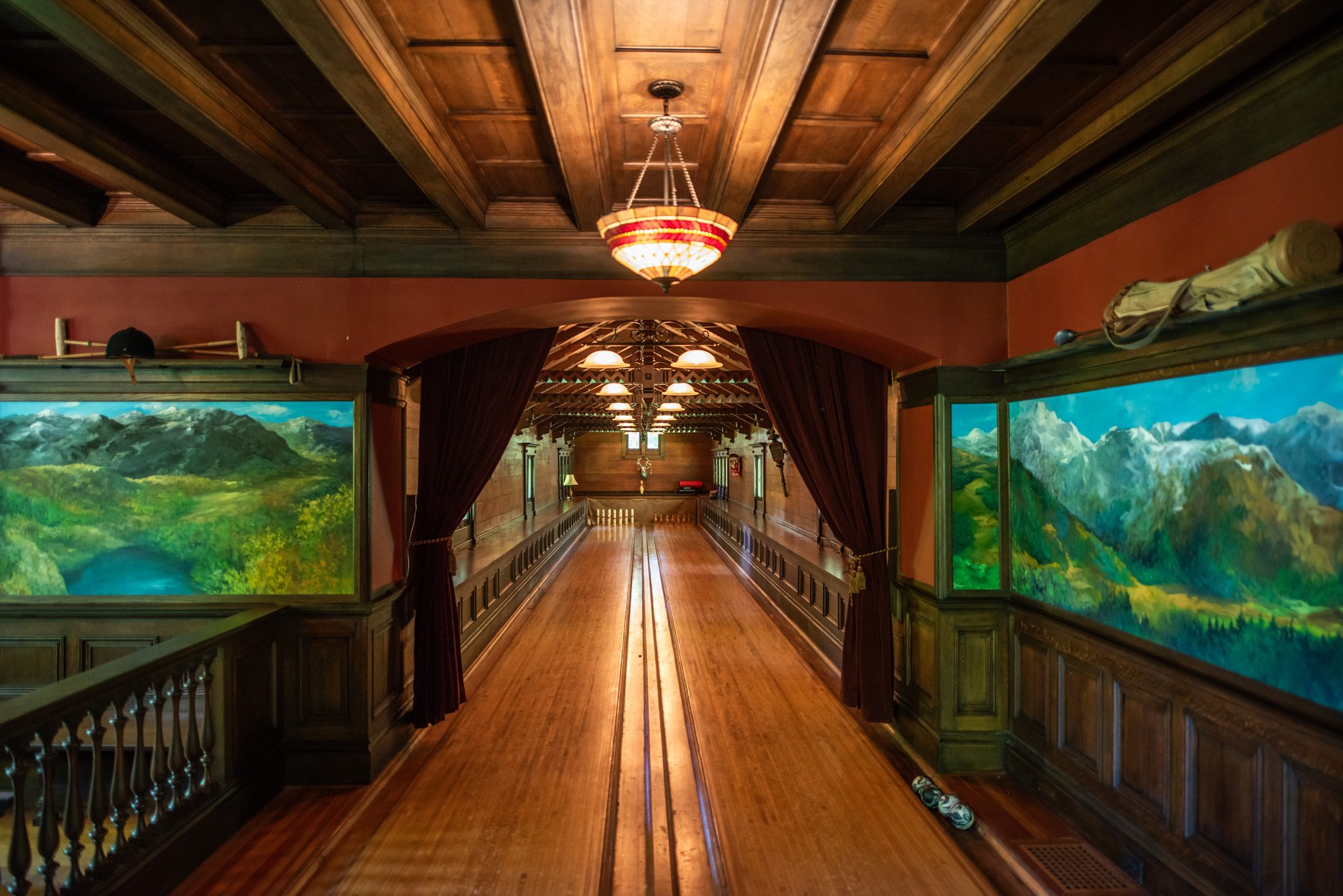 Inside, two polished wooden lanes run between painted alpine murals under a beamed ceiling and a glass pendant.