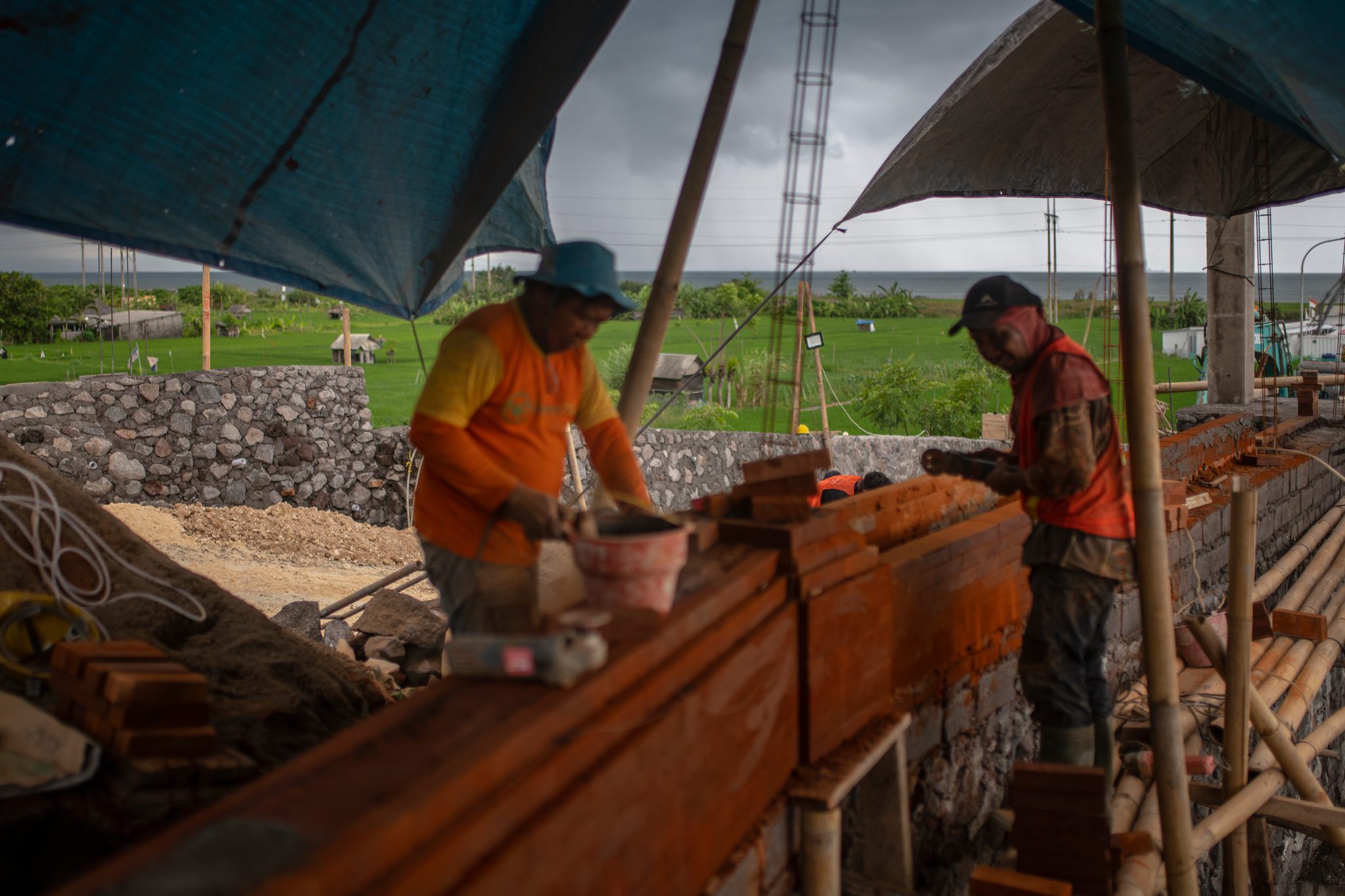 Beneath the tarps, two workers move along the wooden trough together.