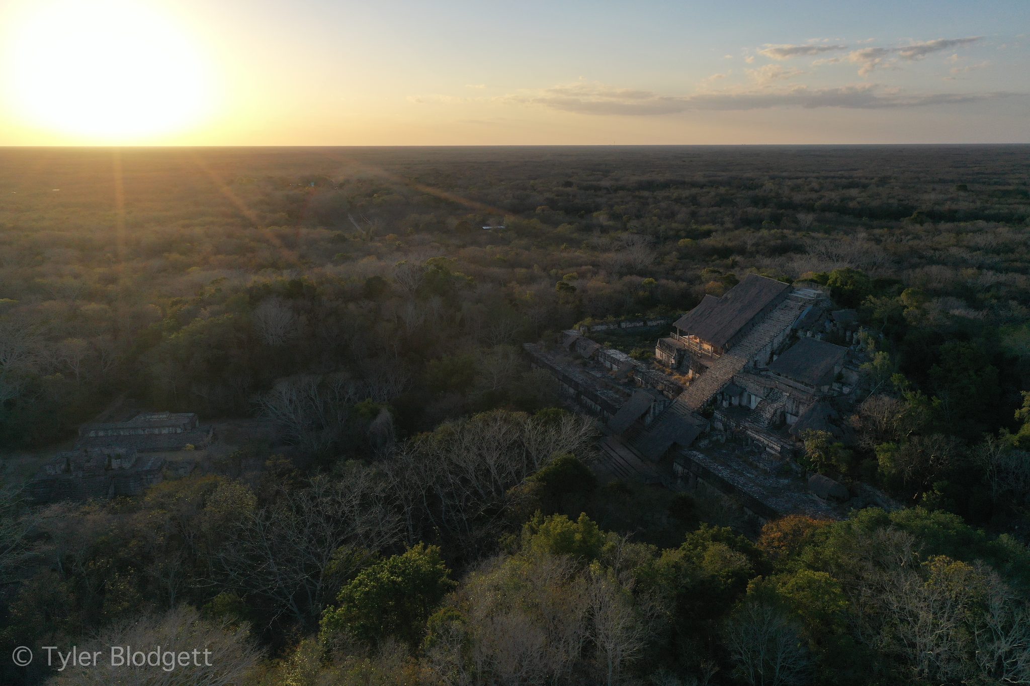 The sun sets over the forest canopy, an old stone complex hidden among the trees.
