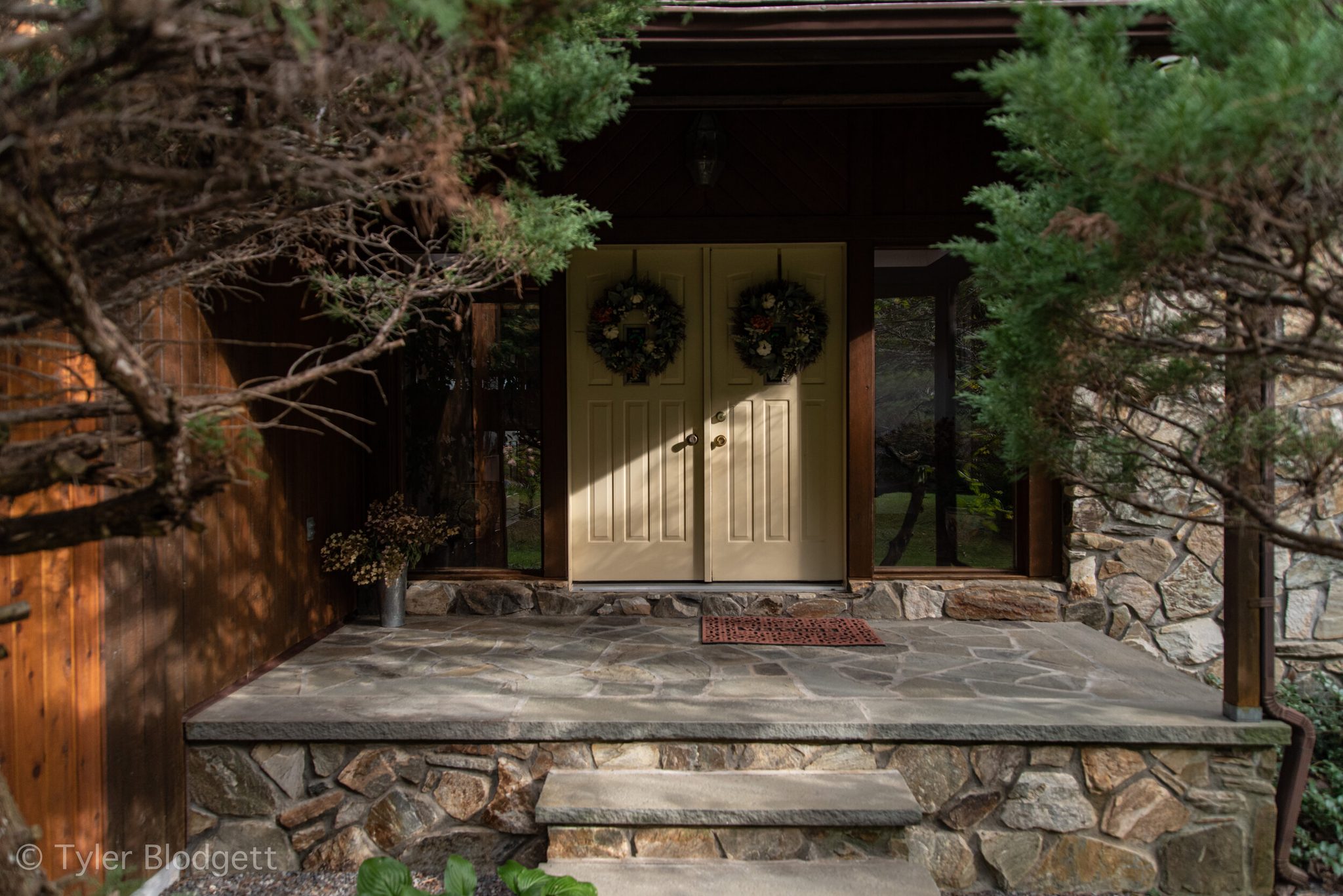 Twin wreaths welcome visitors to a flagstone porch sheltered by the pines.