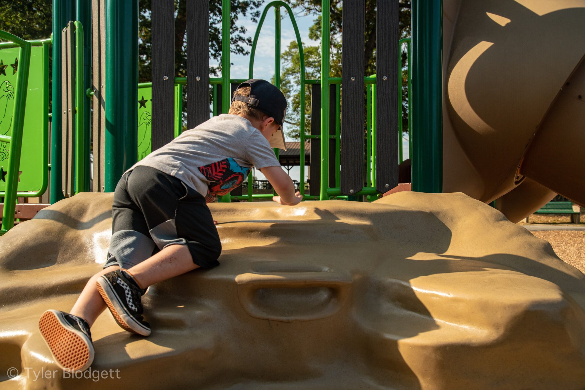 A boy scrambles up the rock wall on hands and knees.
