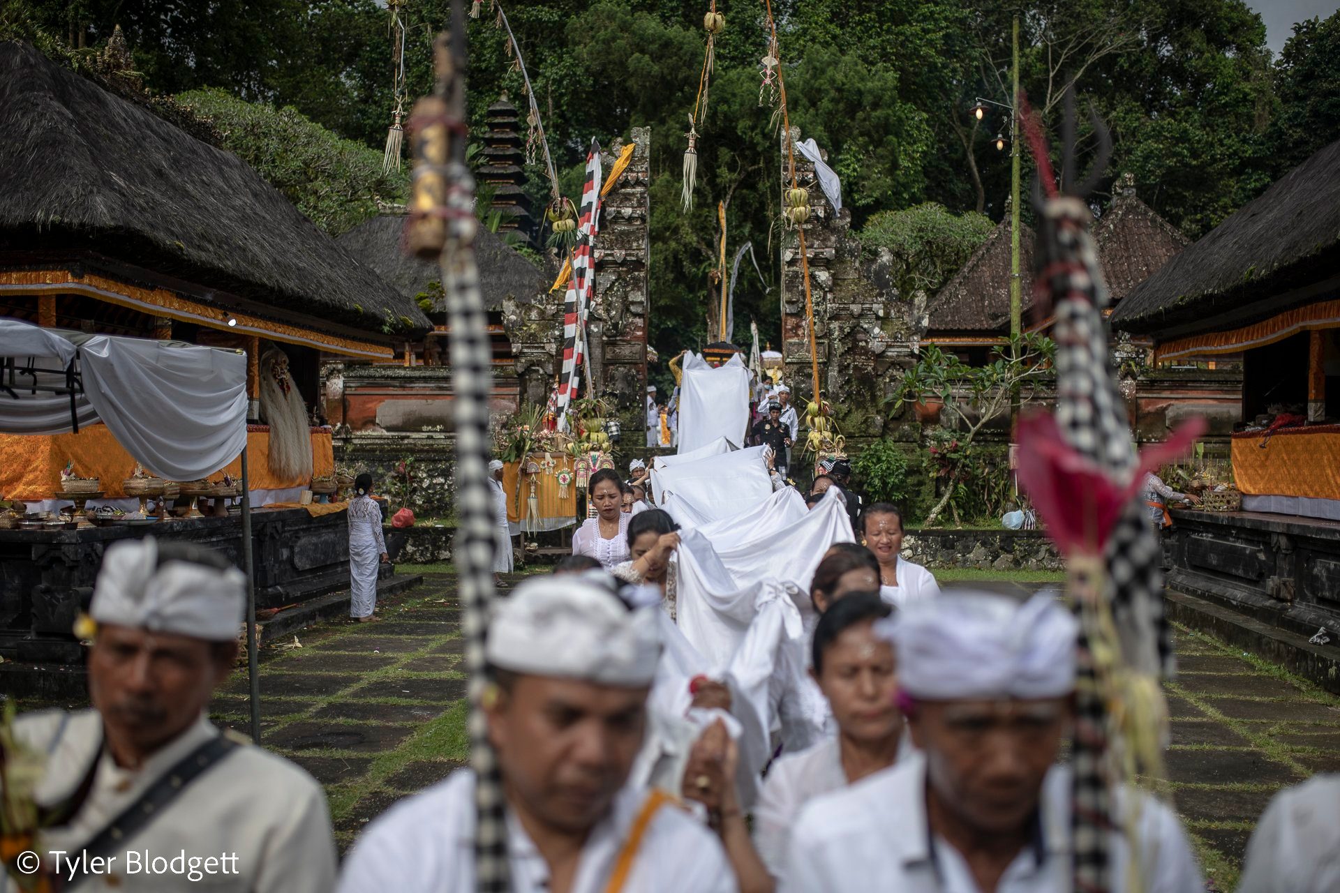A long white cloth is carried through the courtyard, the procession walking beneath it.
