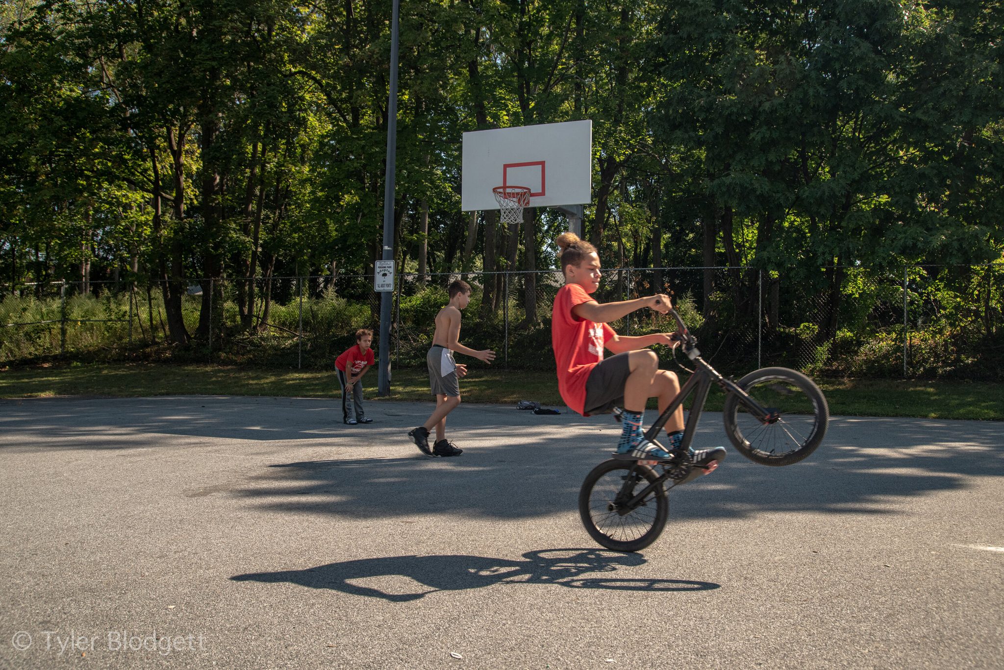 A boy pops a wheelie across the basketball court while his friends shoot around.