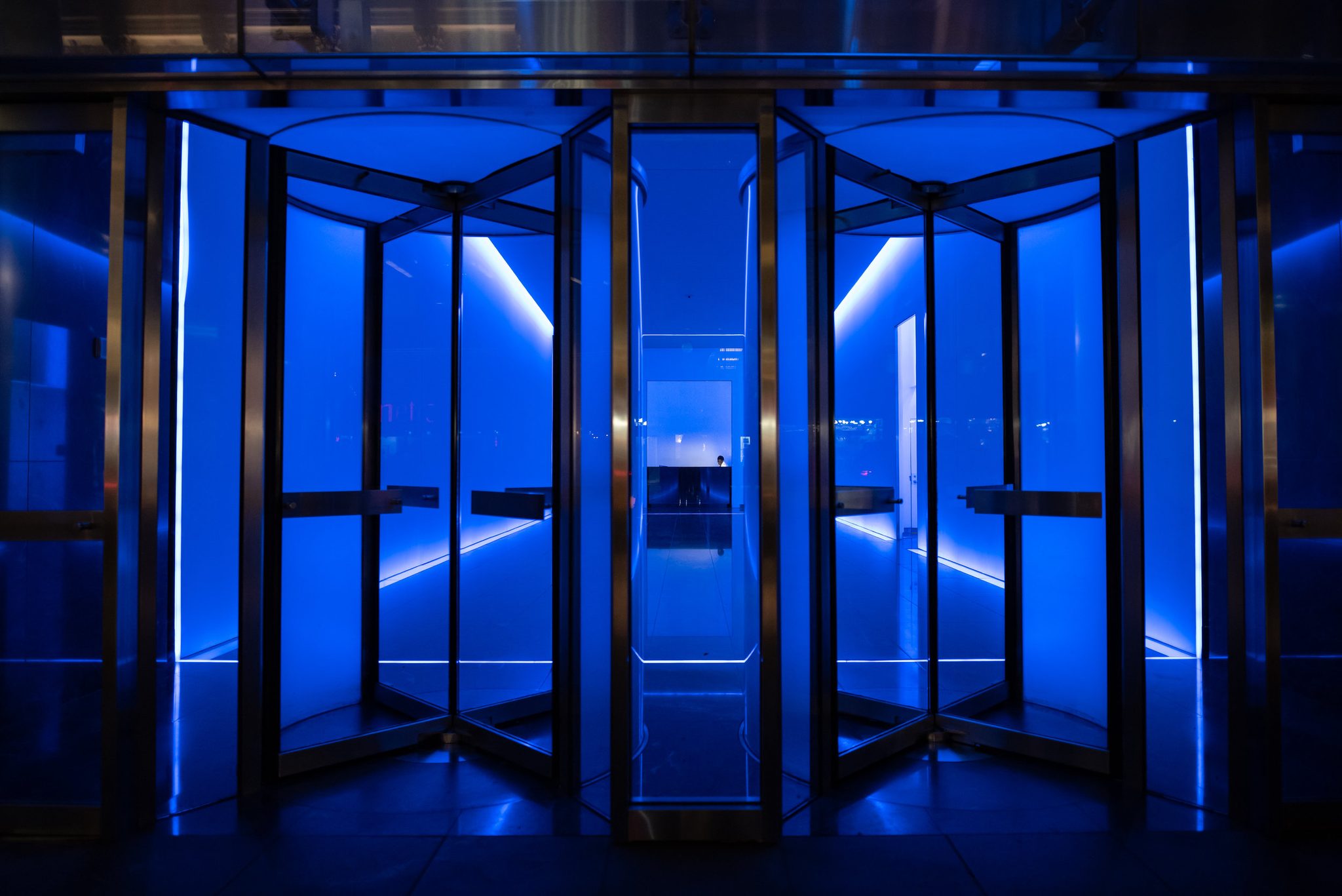 Revolving doors glow electric blue in an empty lobby.
