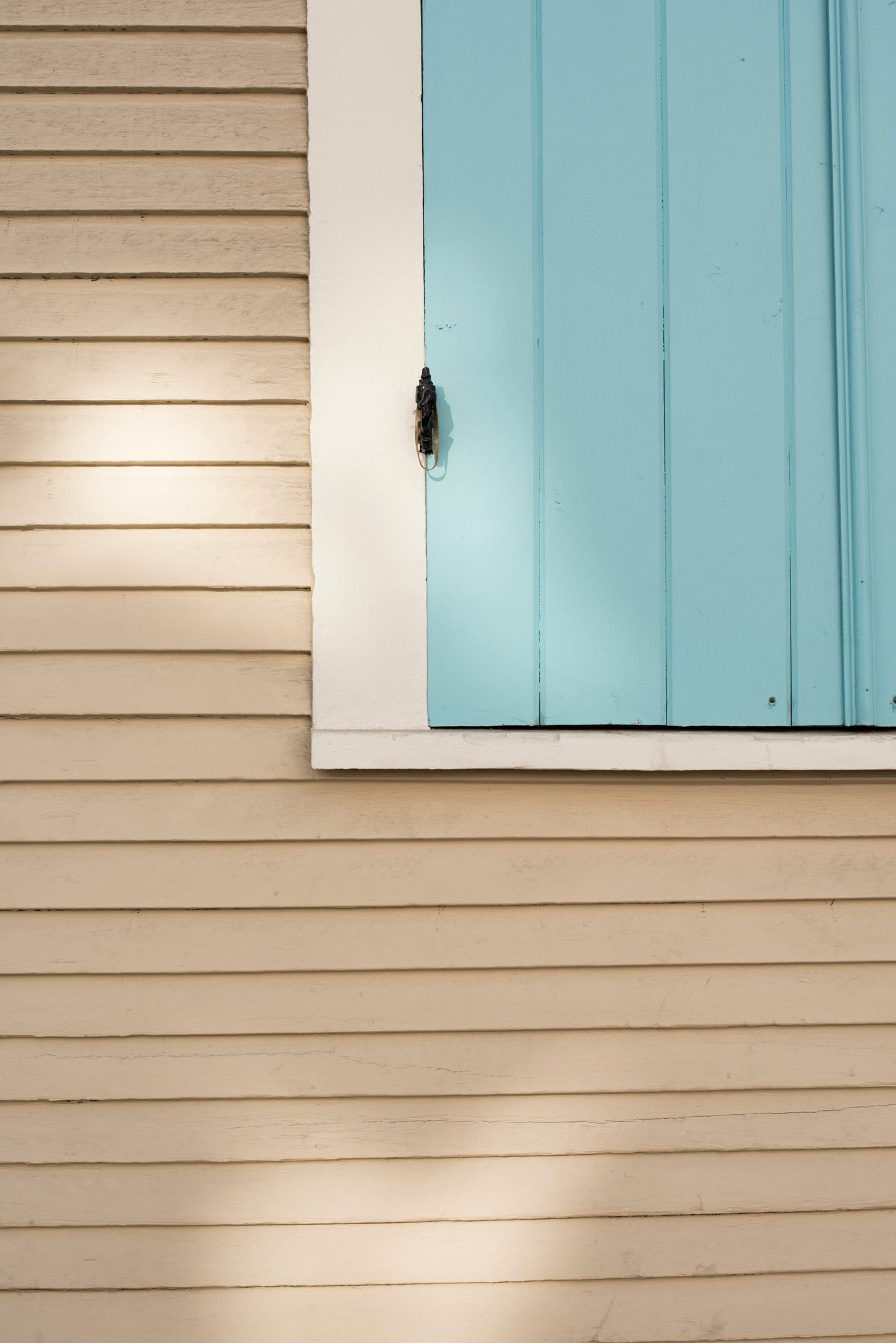 A turquoise shutter against pale yellow clapboard.
