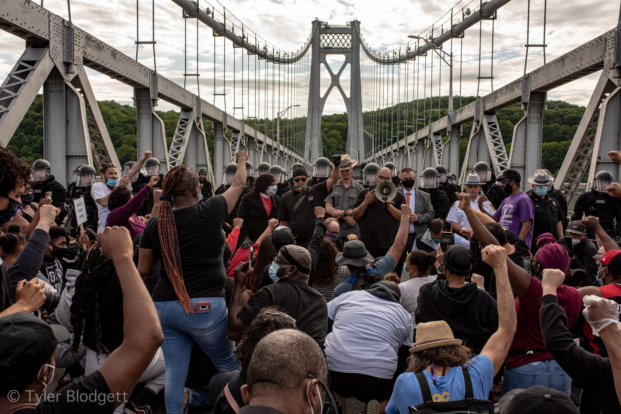 Marchers sit down on the bridge deck in front of the line, fists in the air.