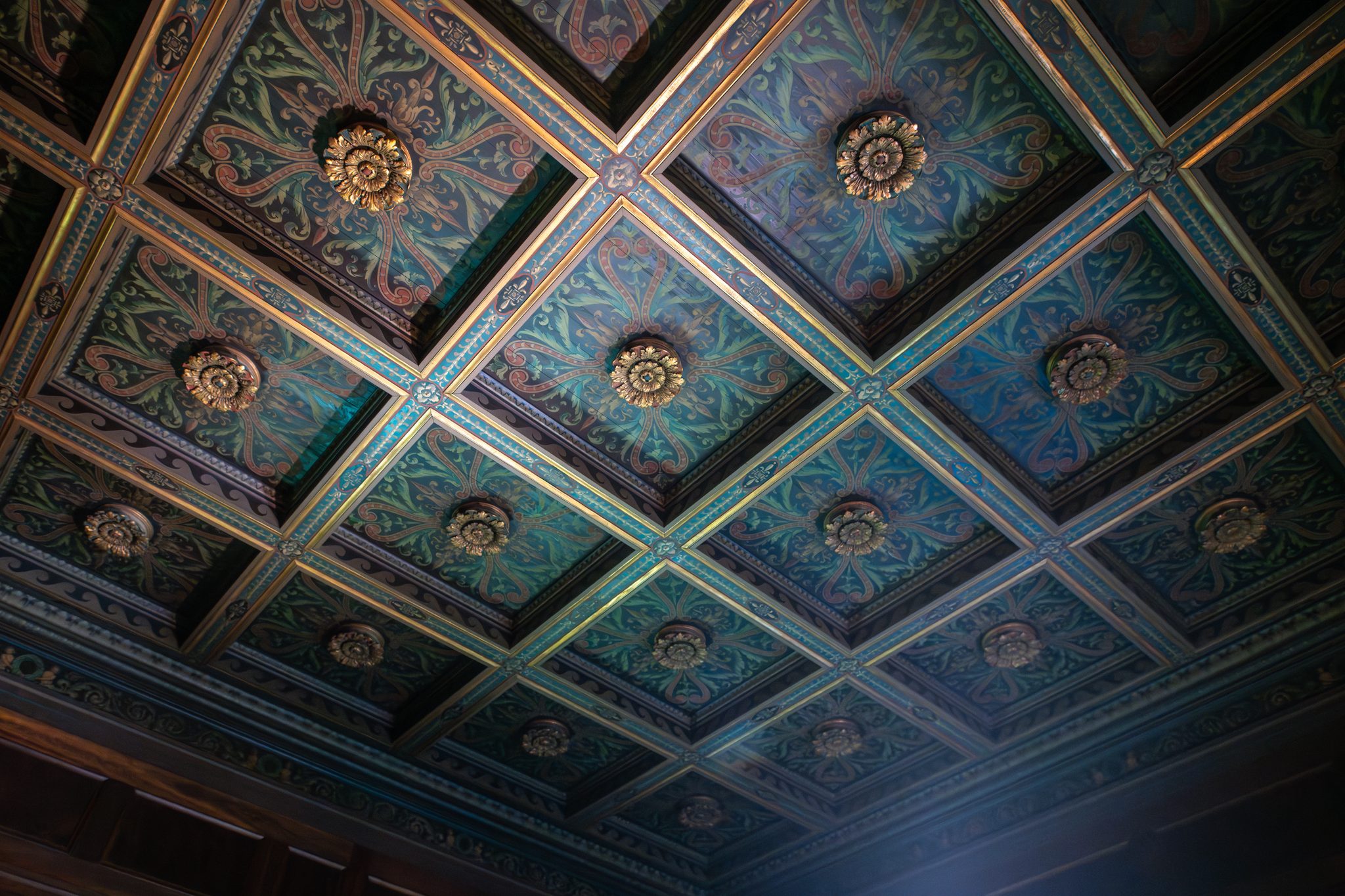 Looking straight up at a painted coffered ceiling, teal and rose panels studded with gilded rosettes.