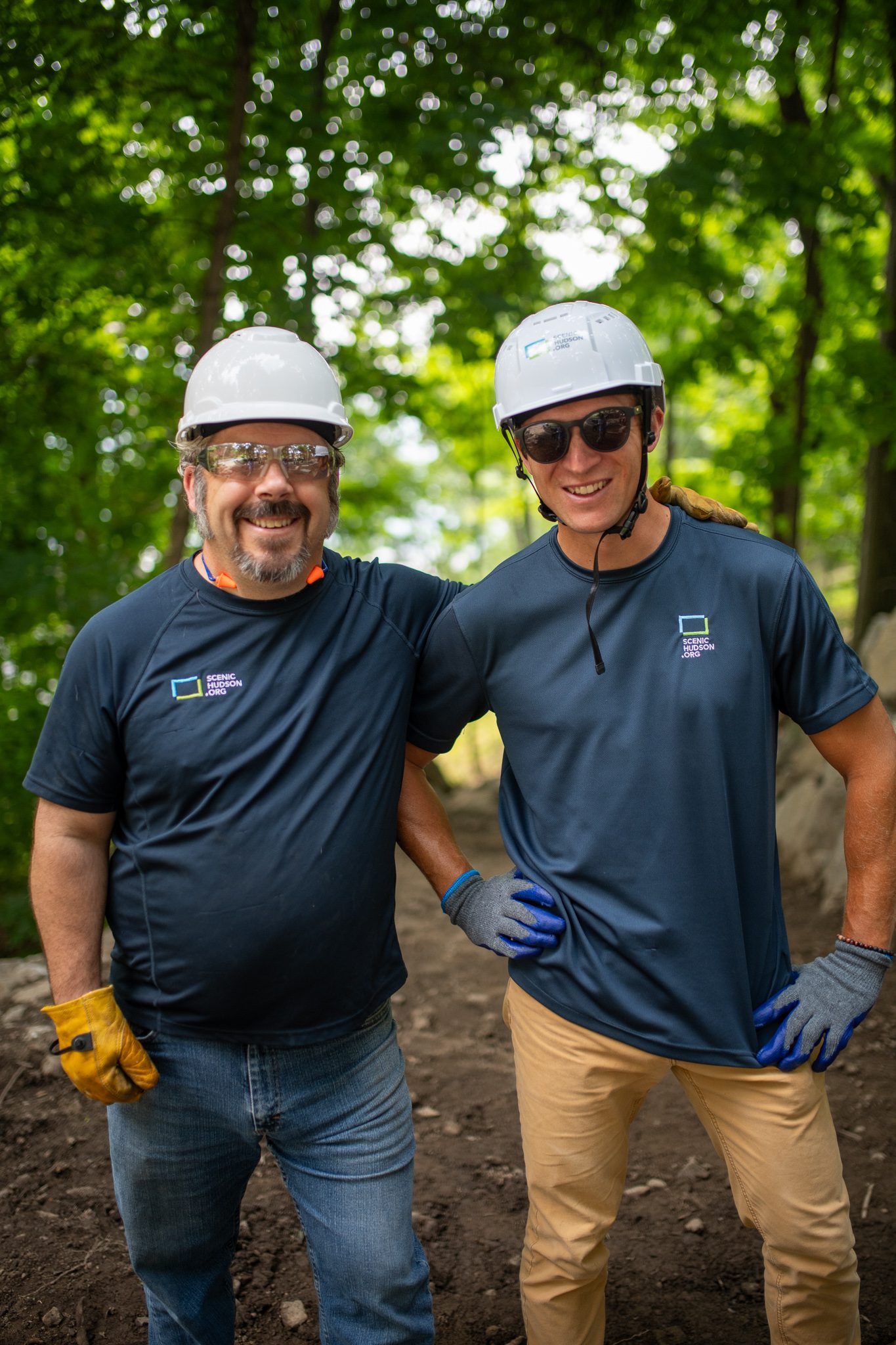 The same pair, hard hats on, hands on hips.