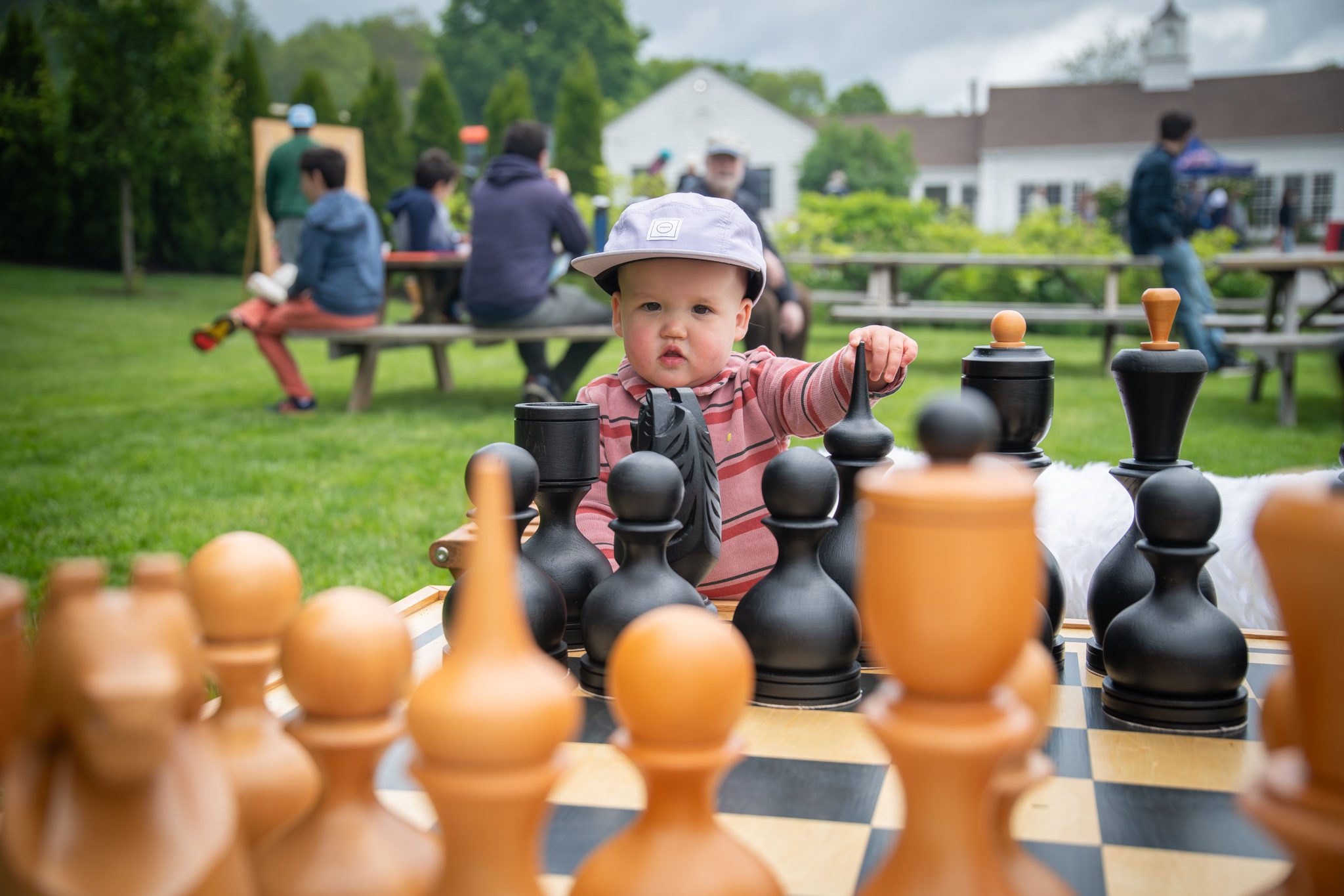 A toddler peeks over the chess pieces, one hand on a black pawn.