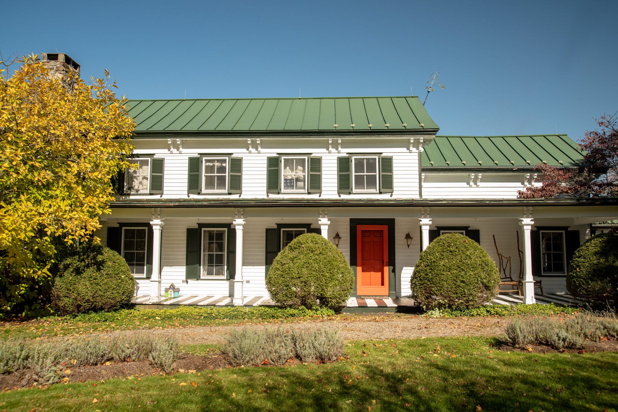 A white farmhouse with a green metal roof and one bright red door.