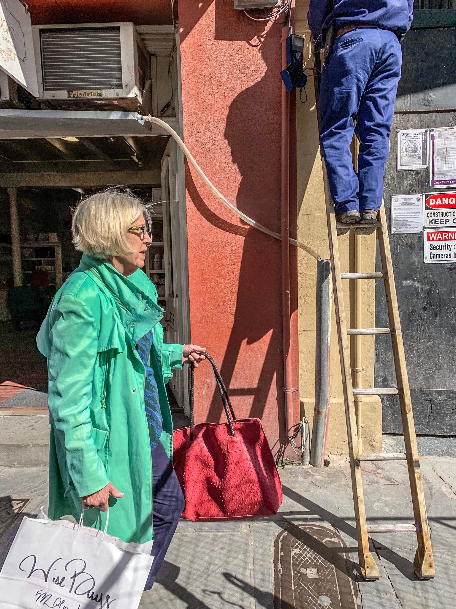 A woman in a green coat walks past a ladder as the work goes on overhead.