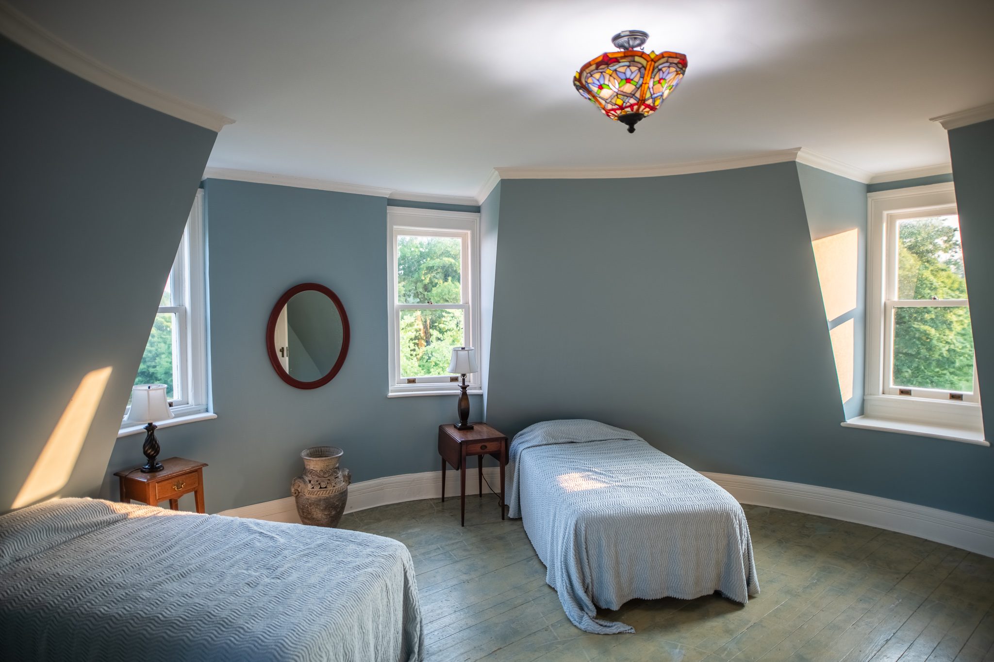 Two twin beds in a pale blue room under the eaves, the sloping walls catching light from dormer windows.