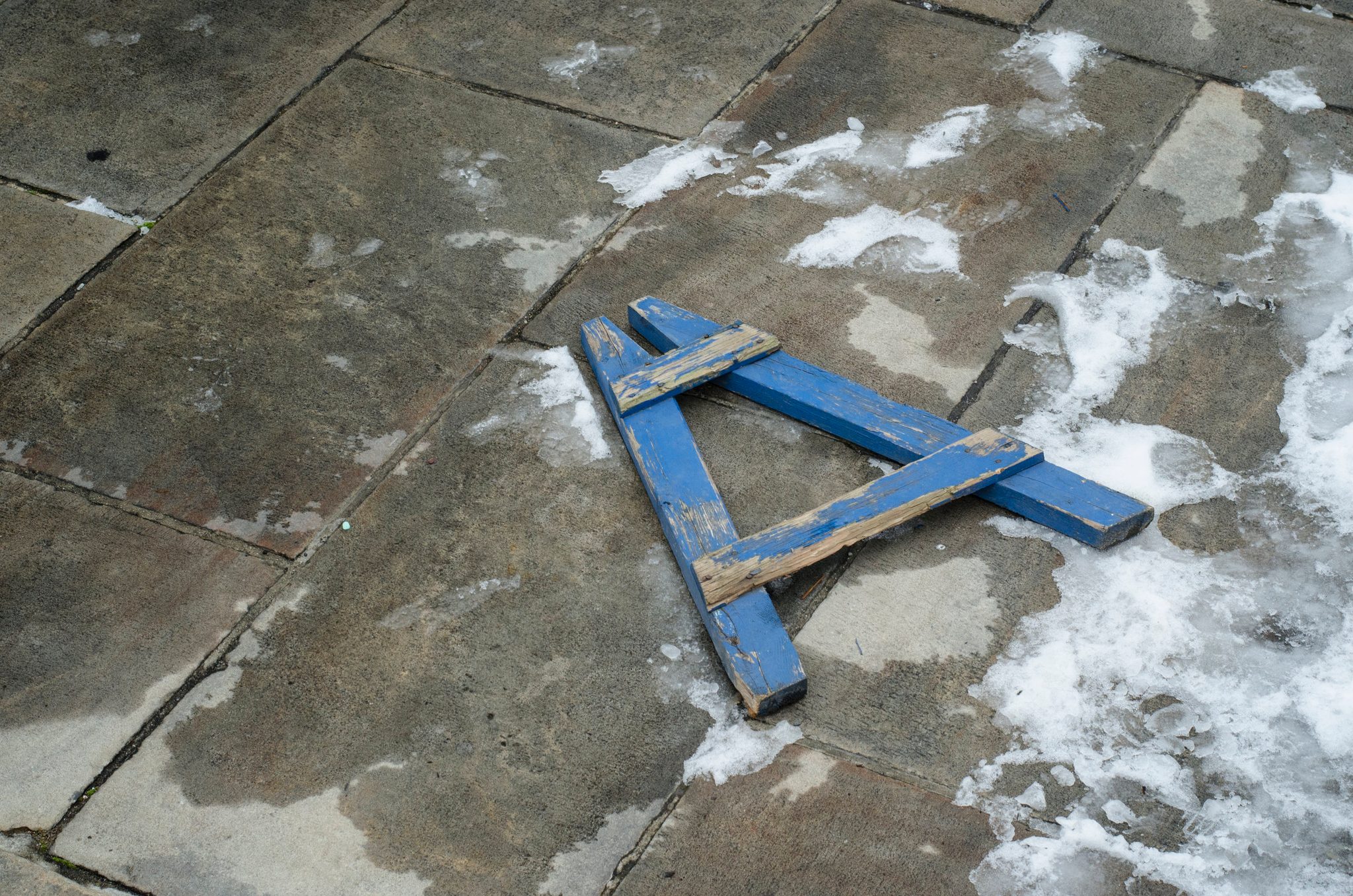 A blue wooden A lies on the snowy flagstones.