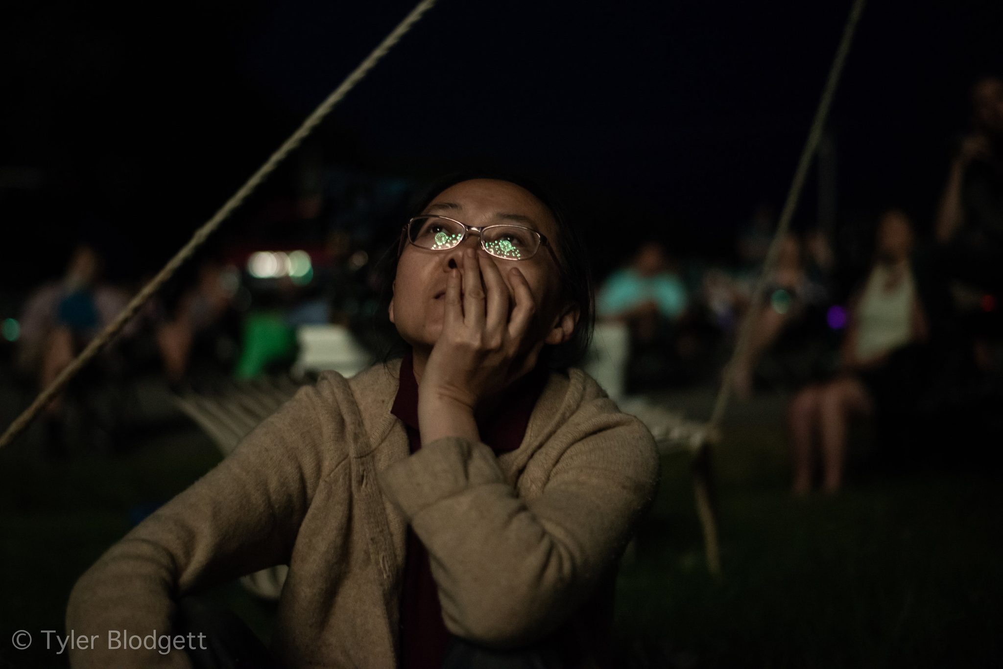 Fireworks flicker in her glasses as she watches with a hand to her cheek.