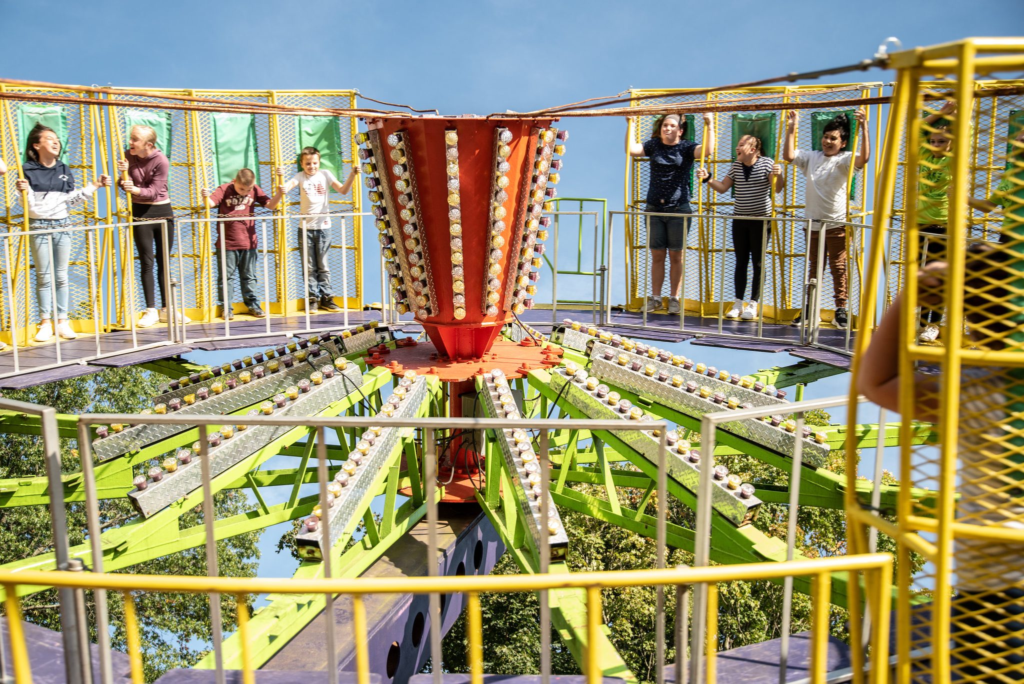Riders wave from the cars of a Ferris wheel painted green and yellow.
