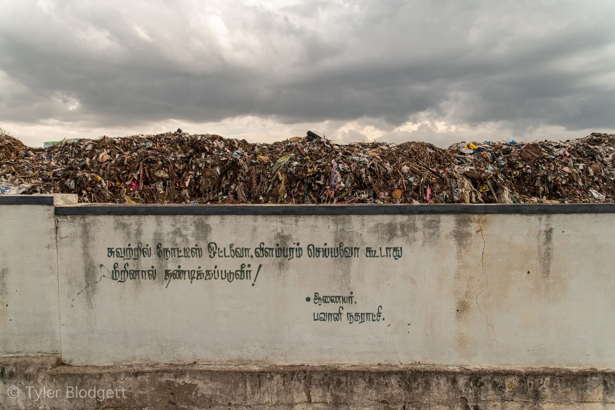 Rubbish piles high behind a wall painted with Tamil lettering.