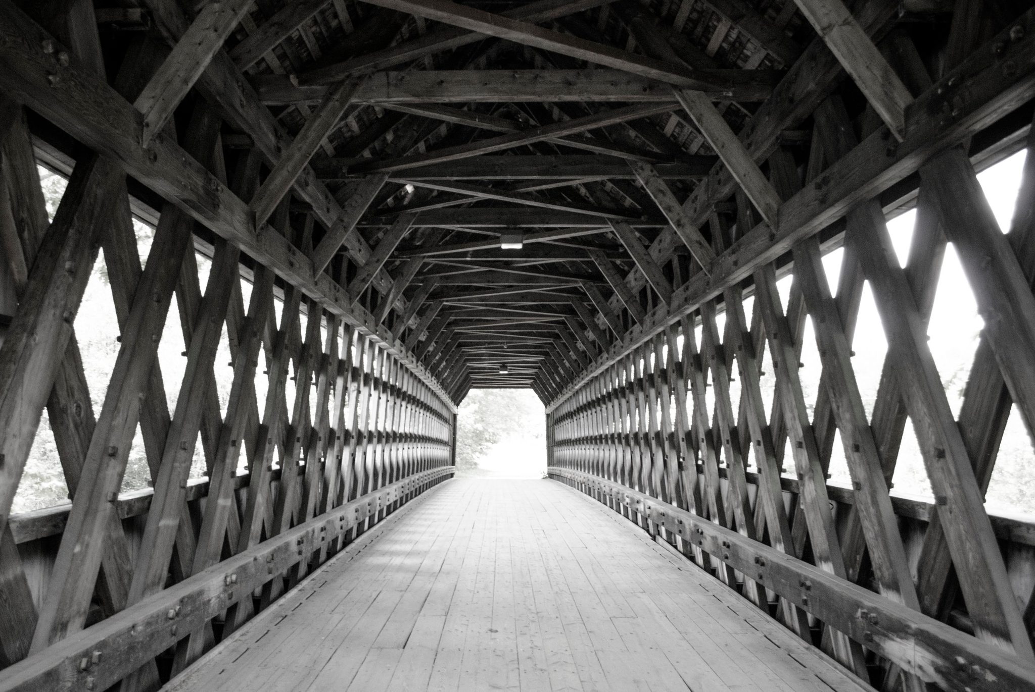 Lattice timbers crisscross the length of a covered bridge, in black and white.
