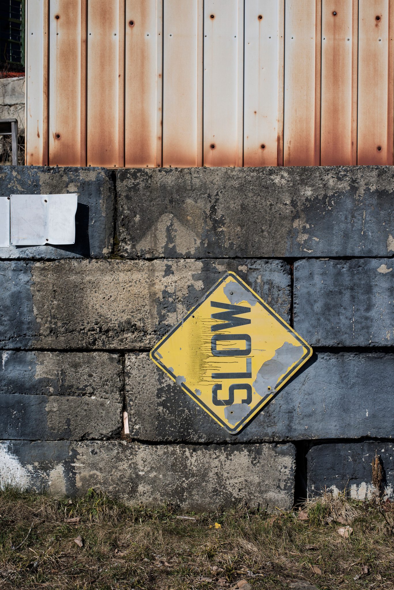 A faded SLOW sign on a block wall beneath rusted siding, taking its own advice.