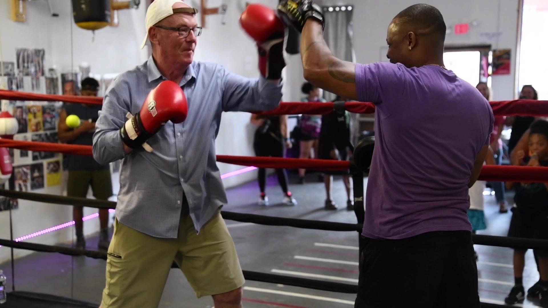 In red gloves, the guest in the button-down throws into the mitts while the crowd lines the ring.