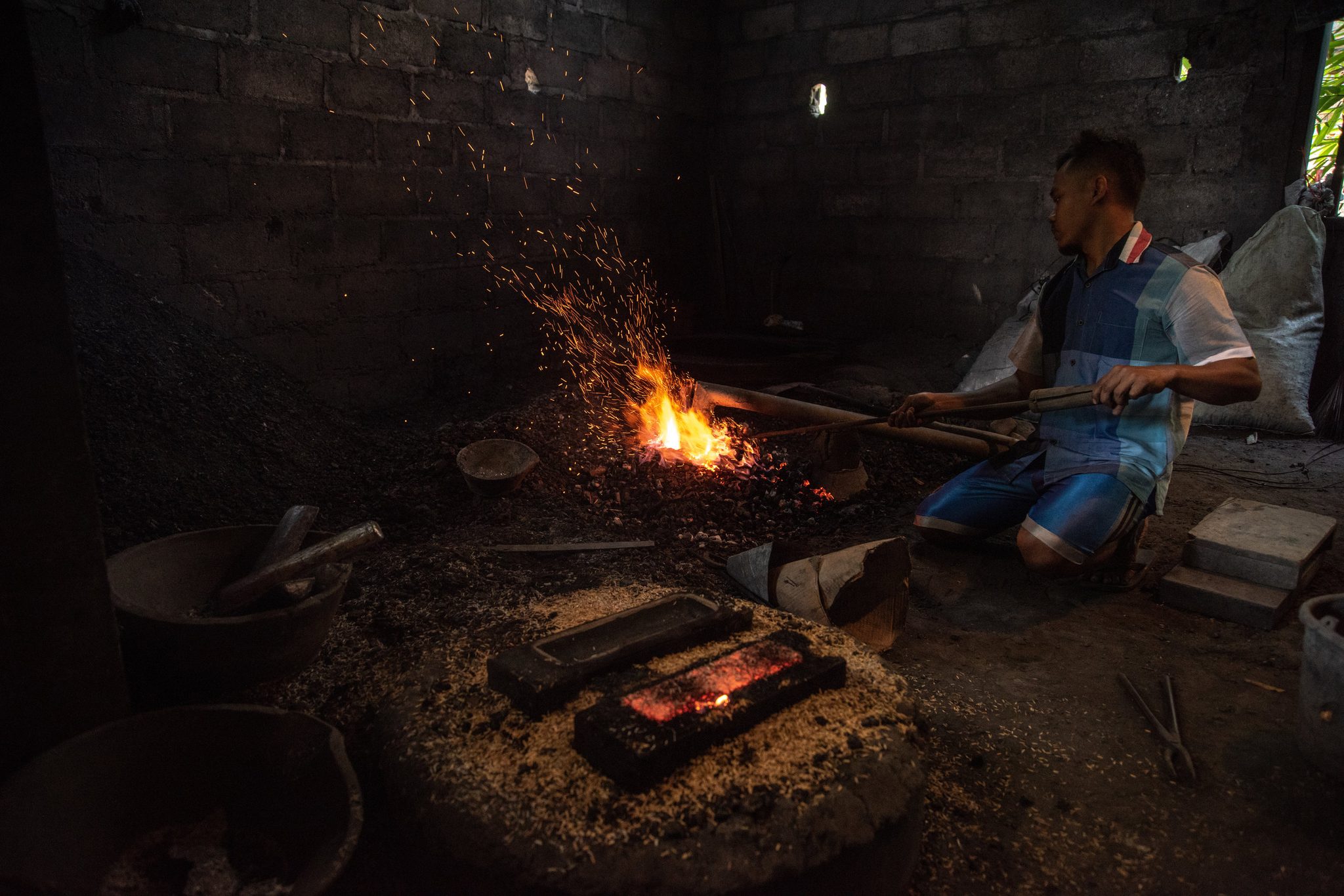 A worker leans into the long handle, feeding air to the fire.
