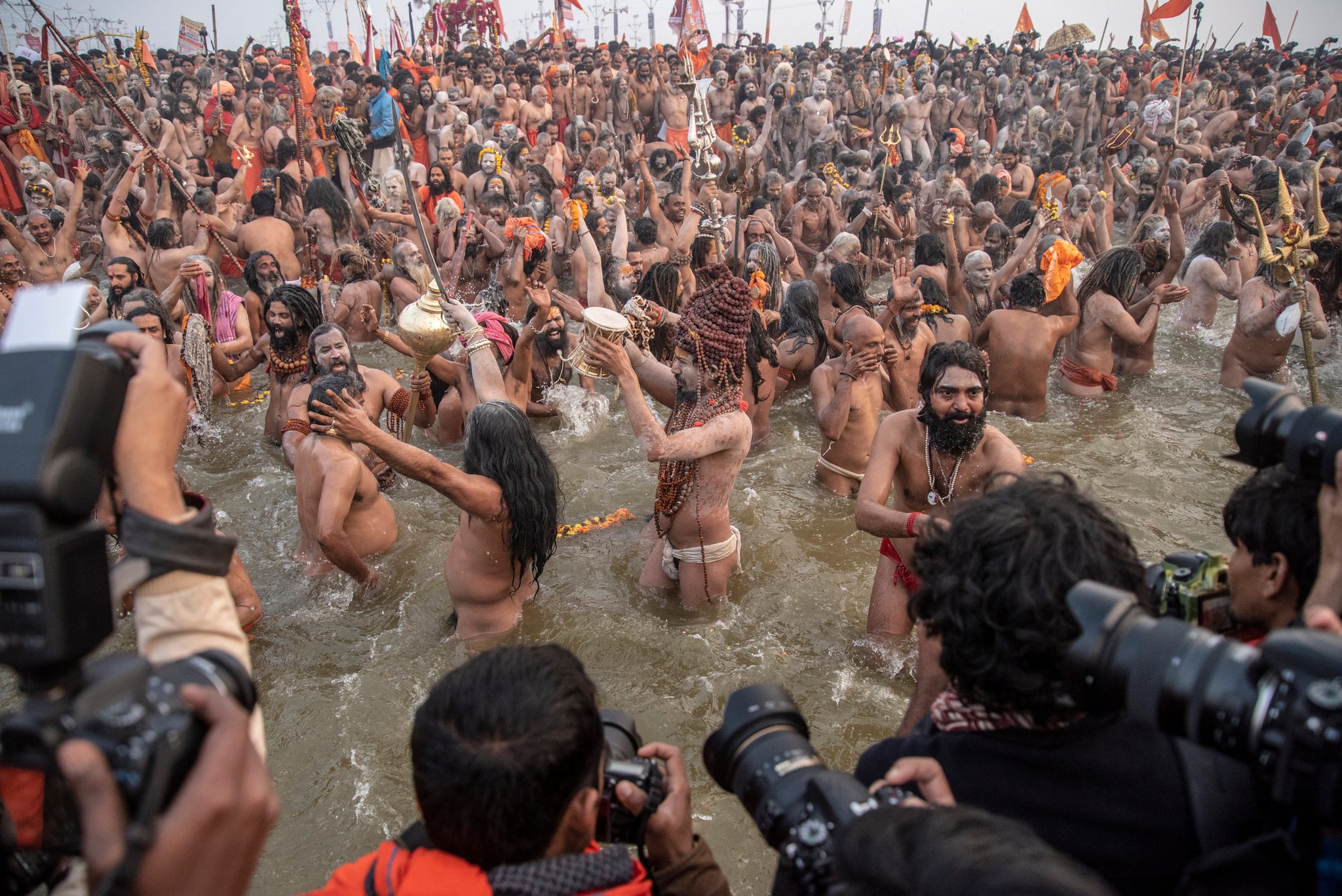 Naga sadhus charge into the river while a wall of cameras records every splash.
