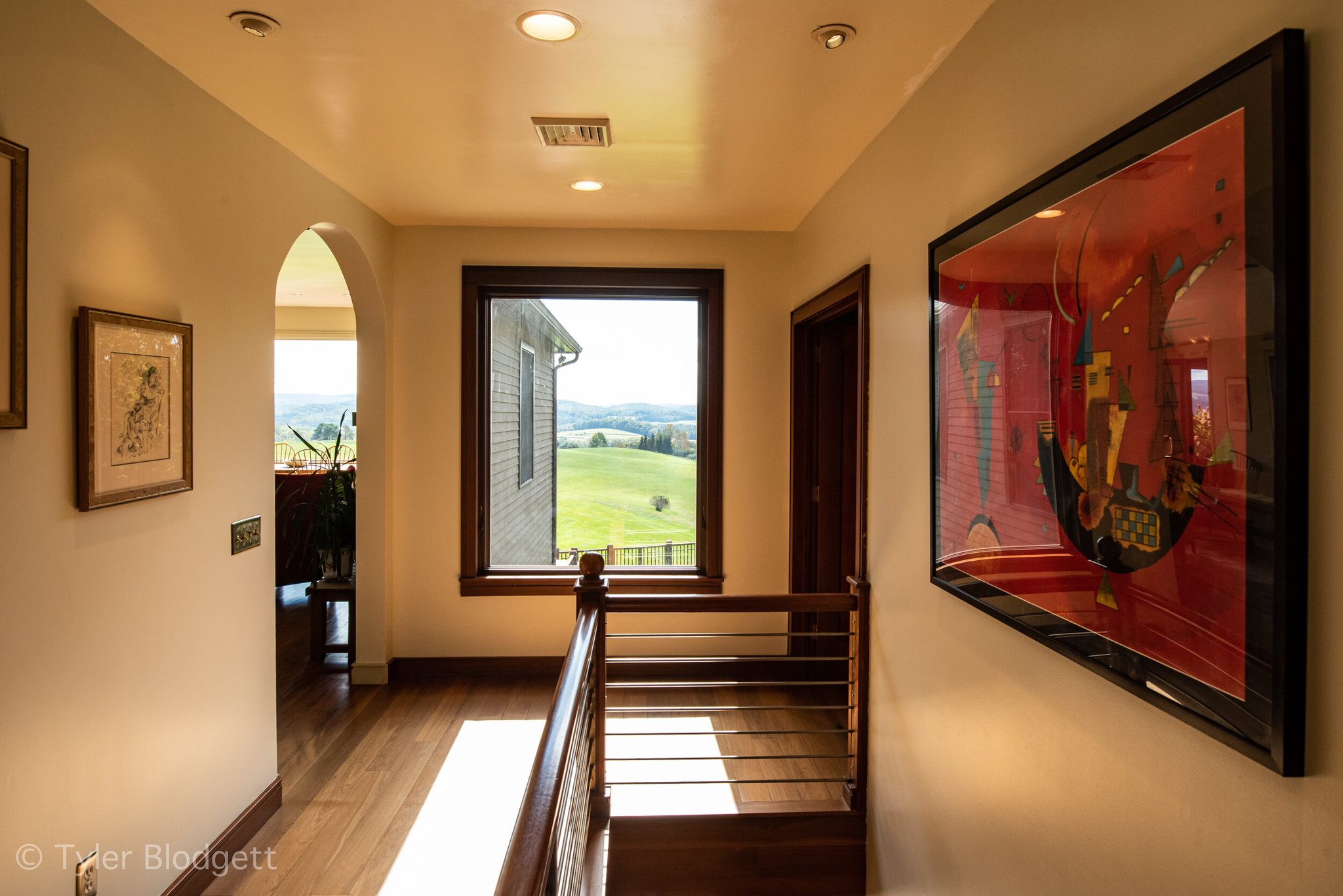 At the top of the stairs, a window frames the rolling farmland like another painting on the wall.