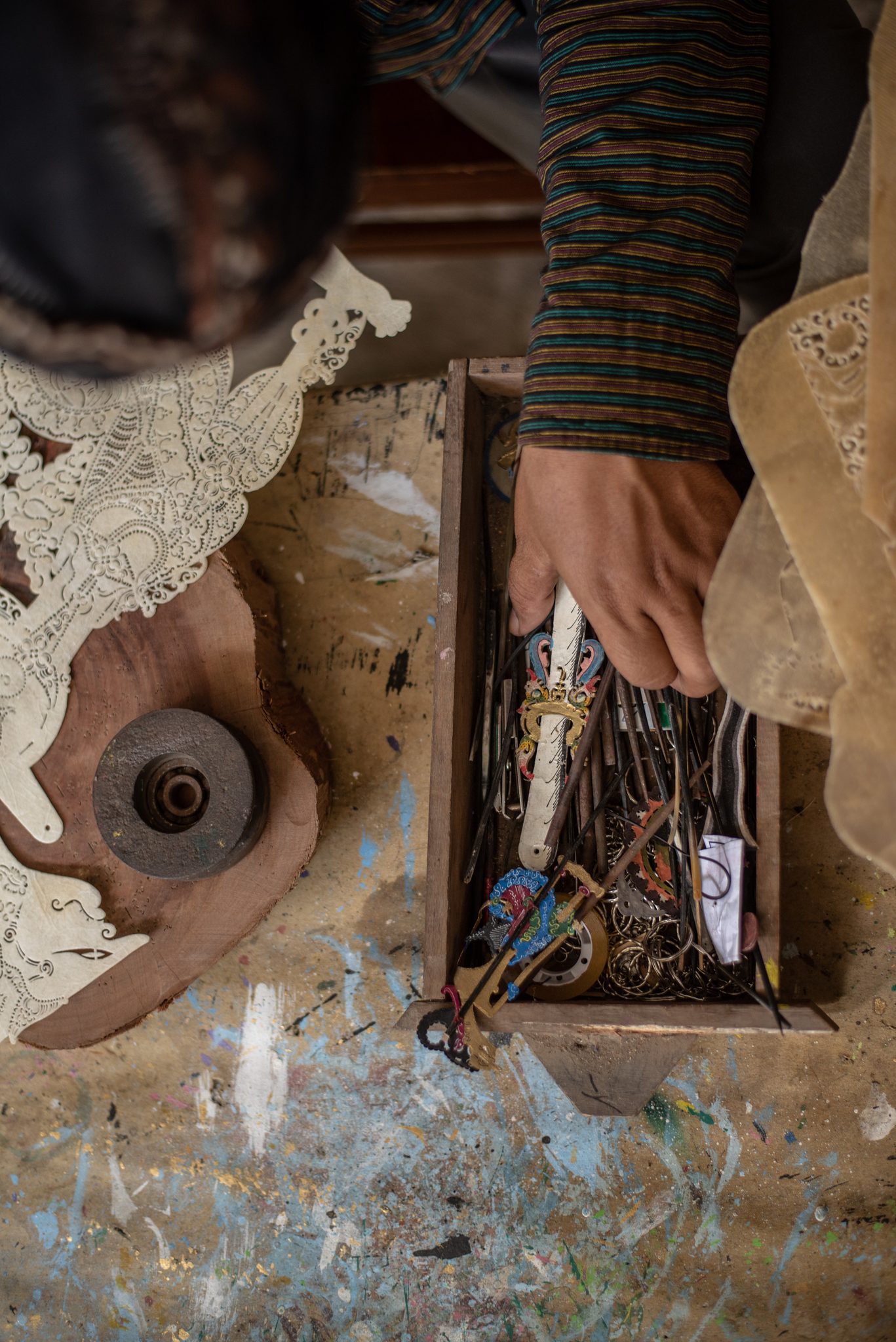 His hand searches the box of chisels while the half-carved puppet waits on the block.