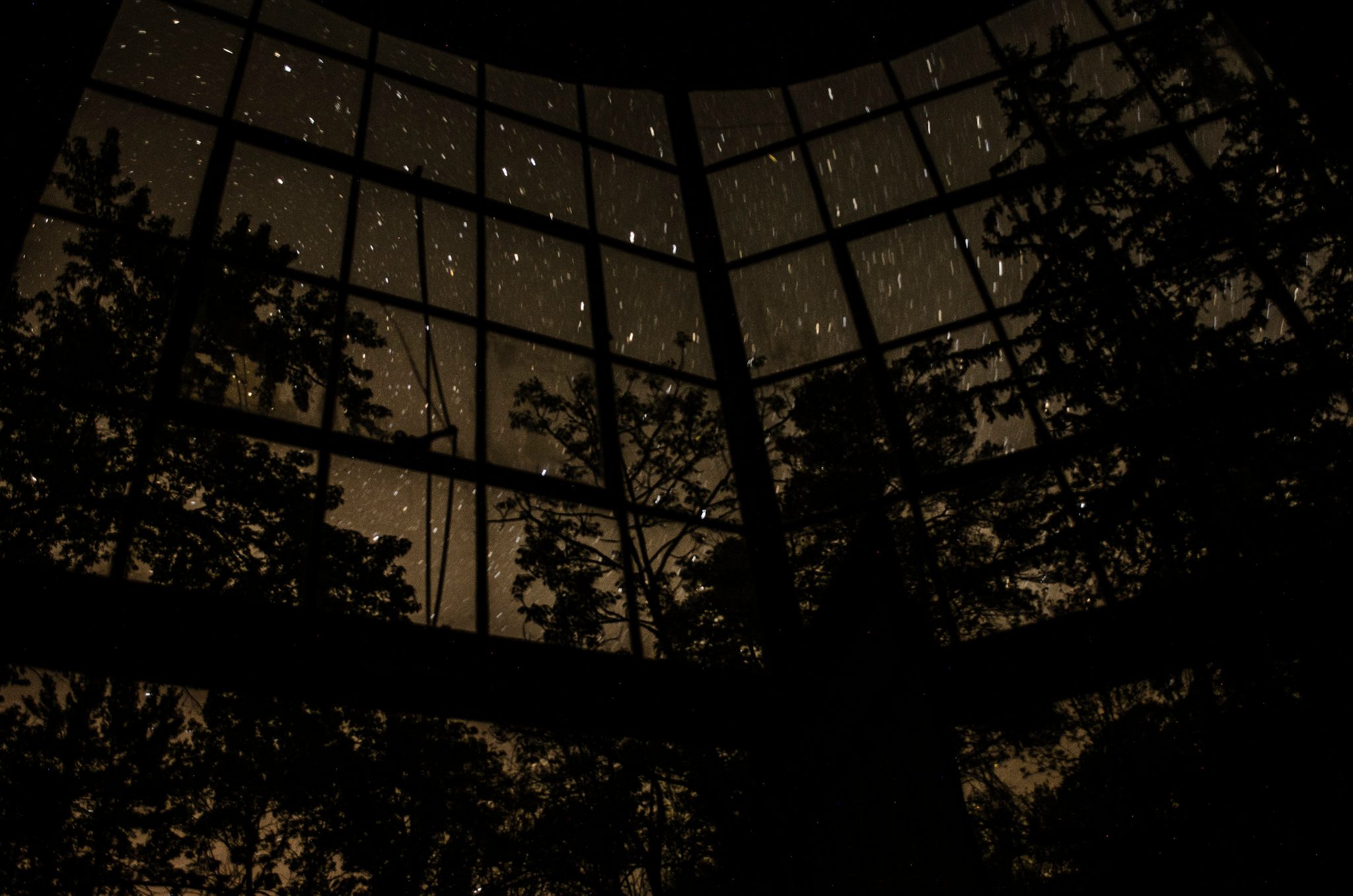 Star trails wheel across the glass dome of a conservatory at night.