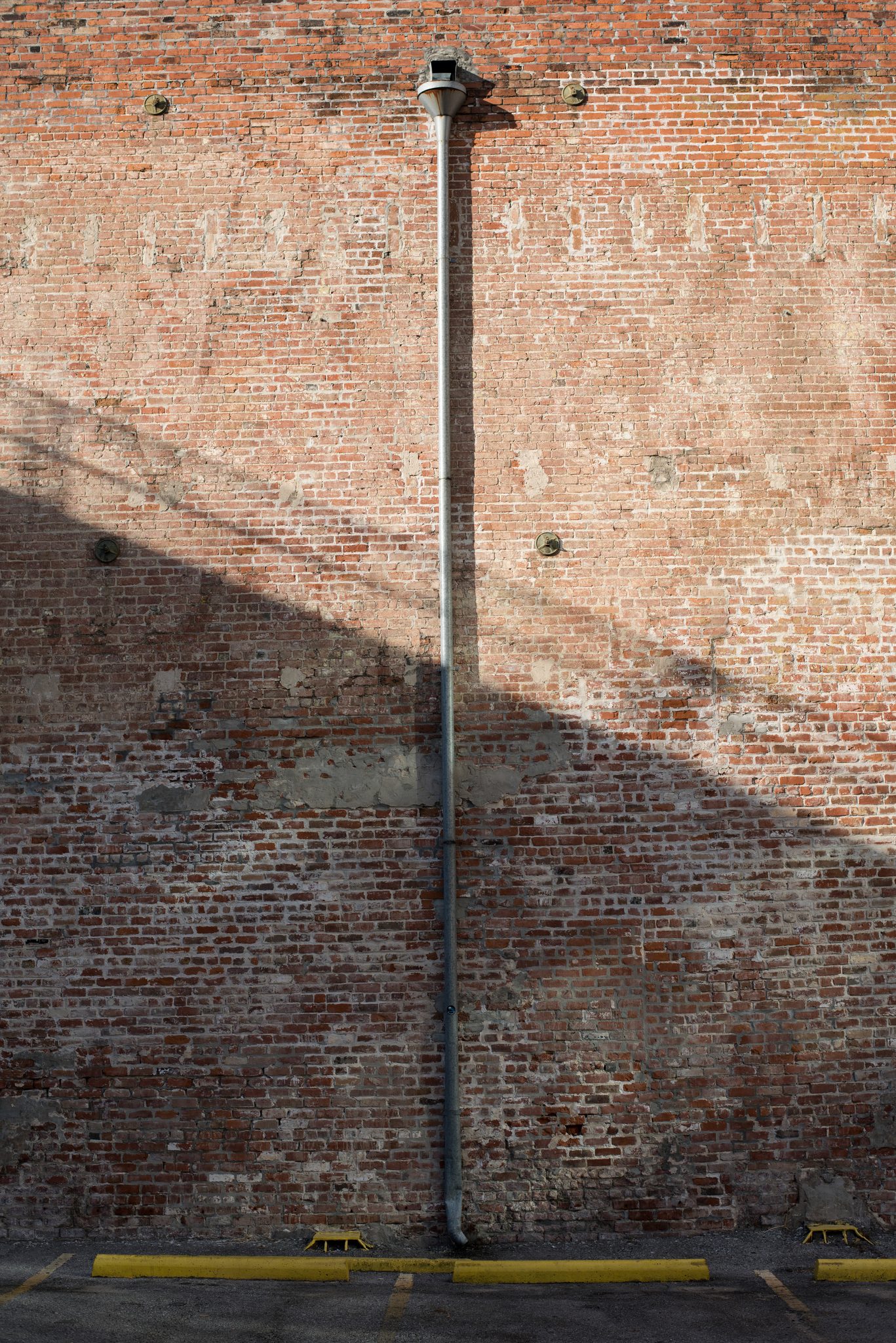 A single drainpipe runs down a weathered brick wall, the light slanting across it.