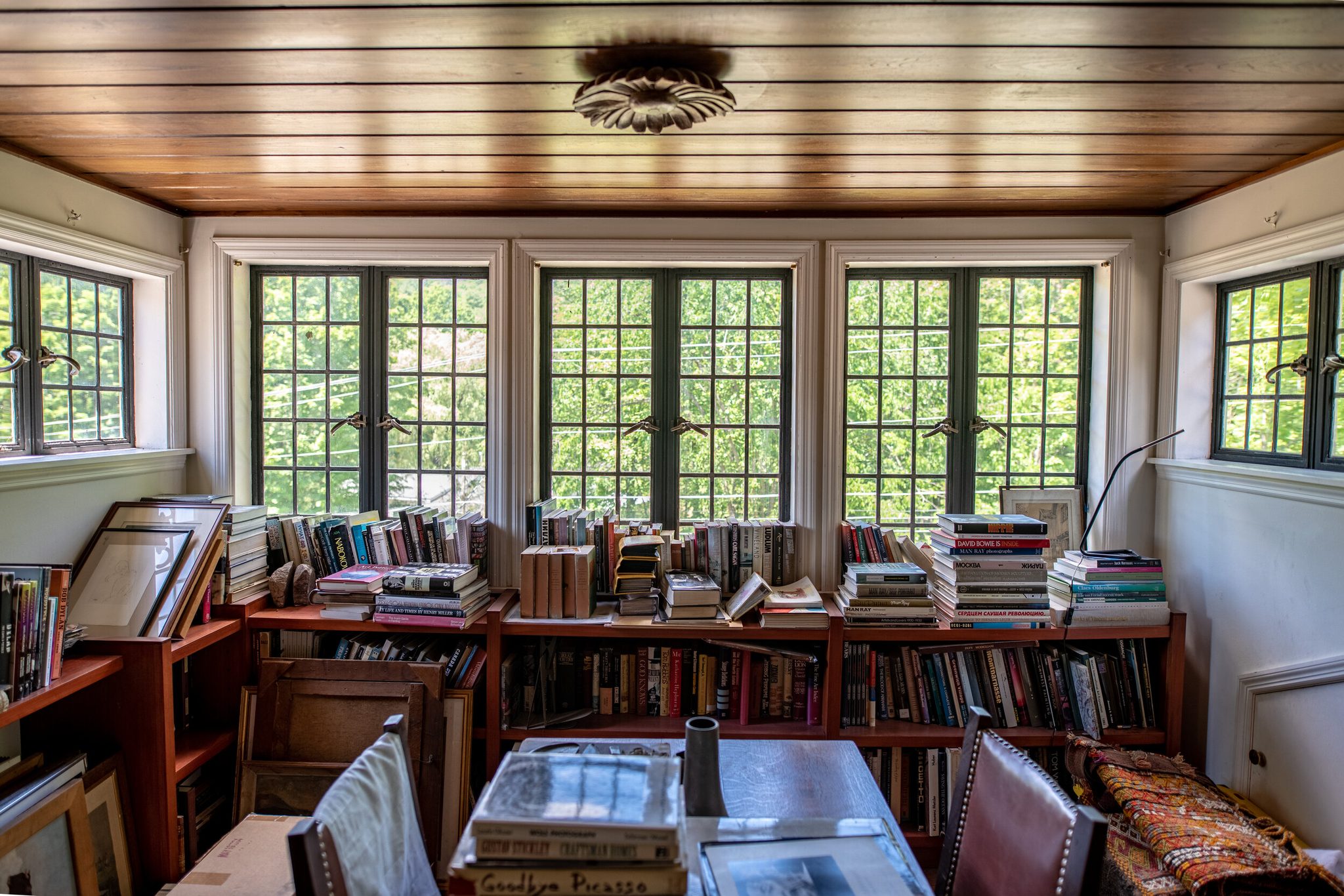 Books pile up on every shelf and table beneath the wall of windows.