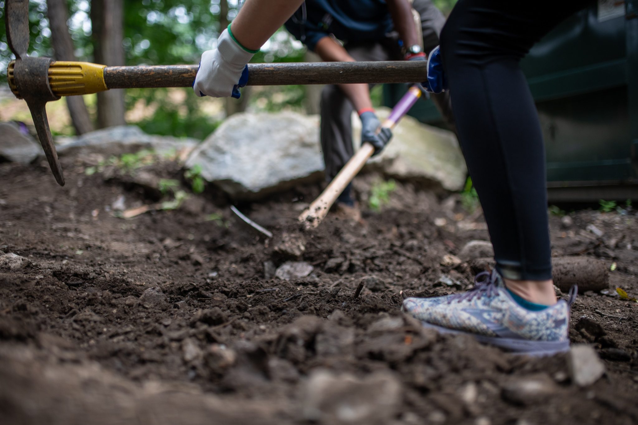 A pick bites into the dirt as another crew member steps past.
