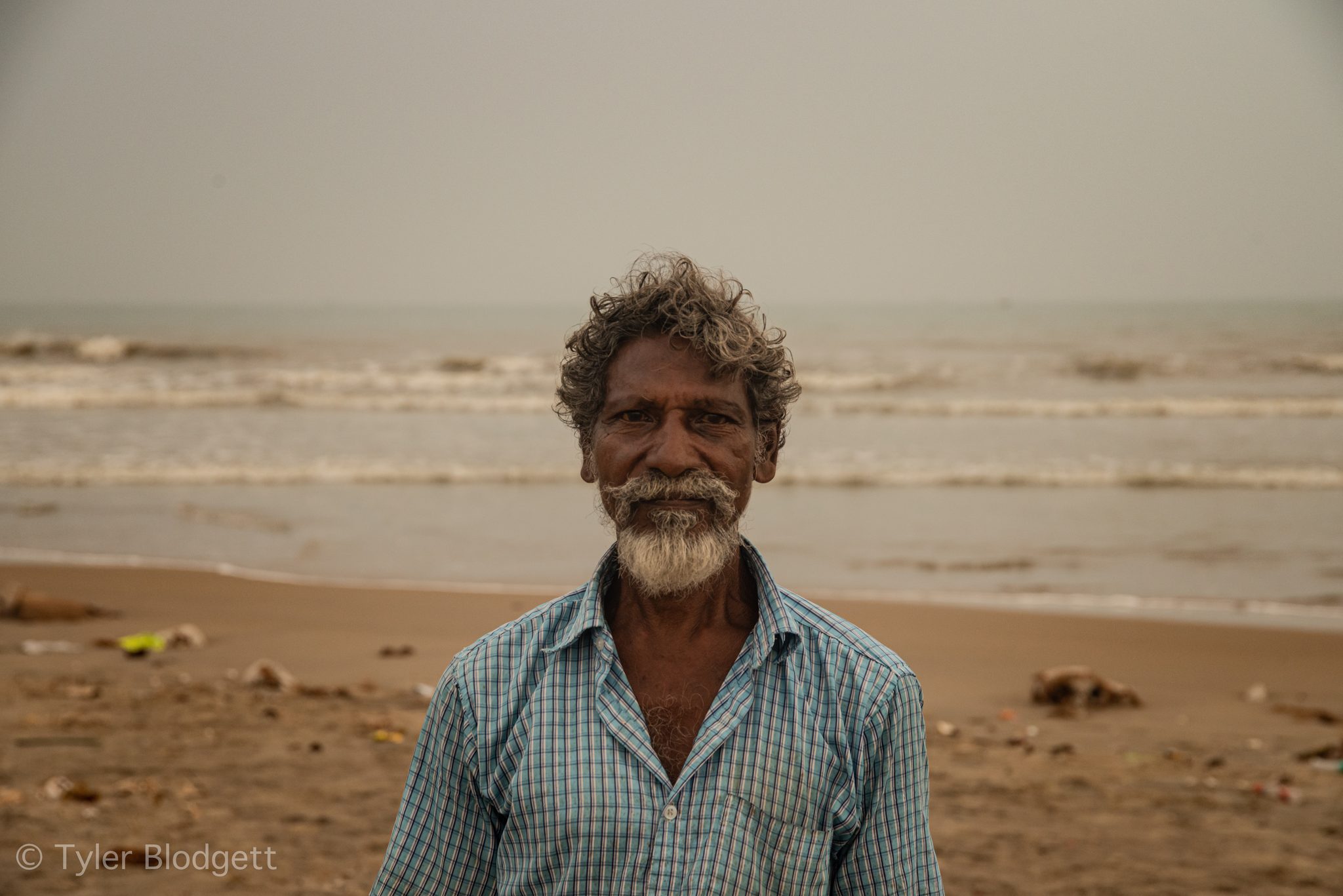 He meets the lens with a small smile, the sea gray behind him.