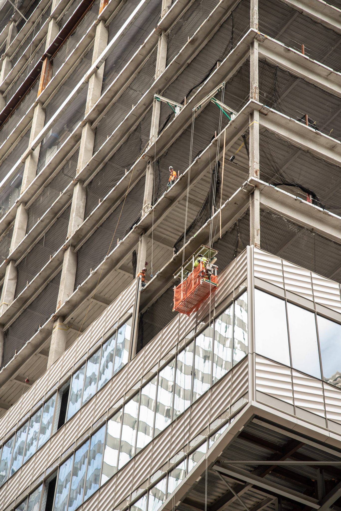 A work platform dangles from the side of a tower still rising in glass.