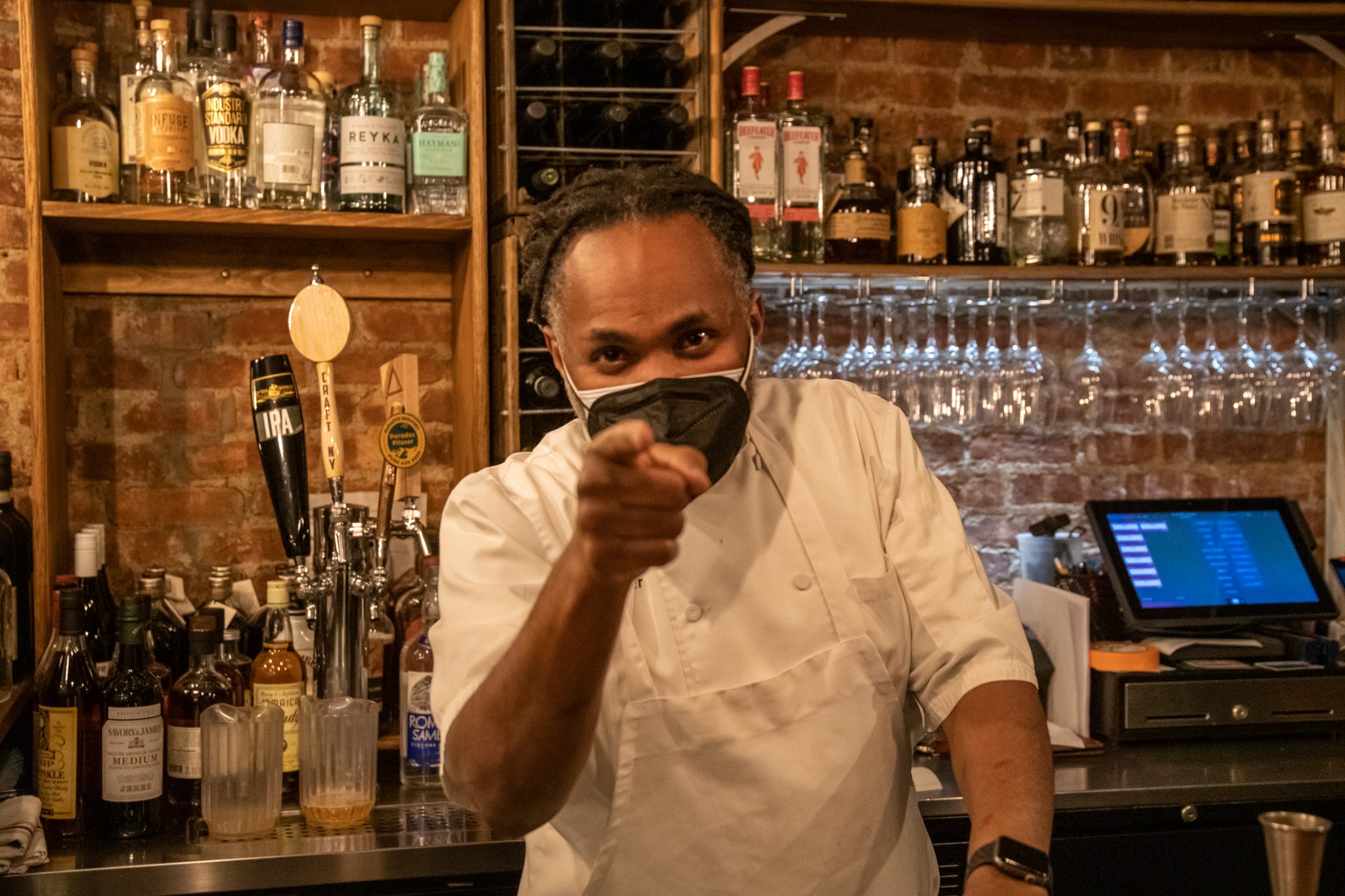 The chef points straight at the camera from behind the bar.