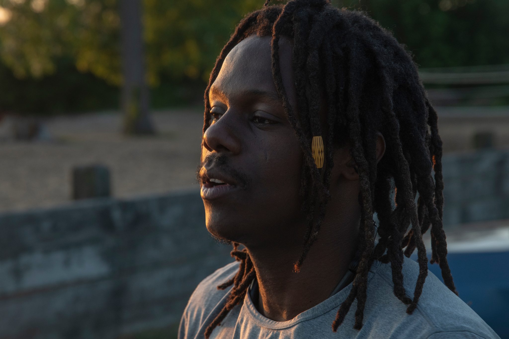 A close portrait in the early light, locs falling past his face, eyes off toward the water.