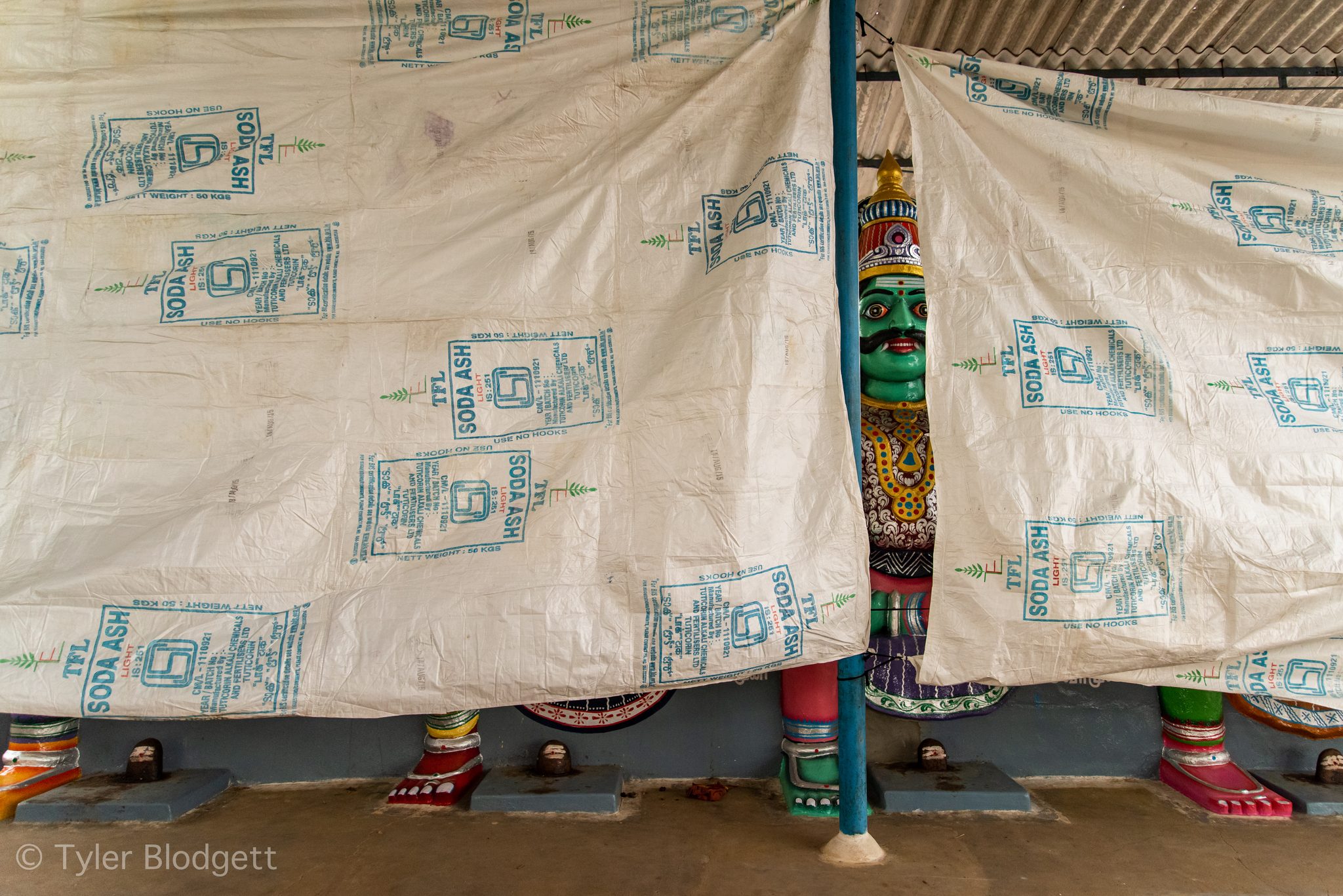 A green-faced deity peeks out from behind a patterned tarp.