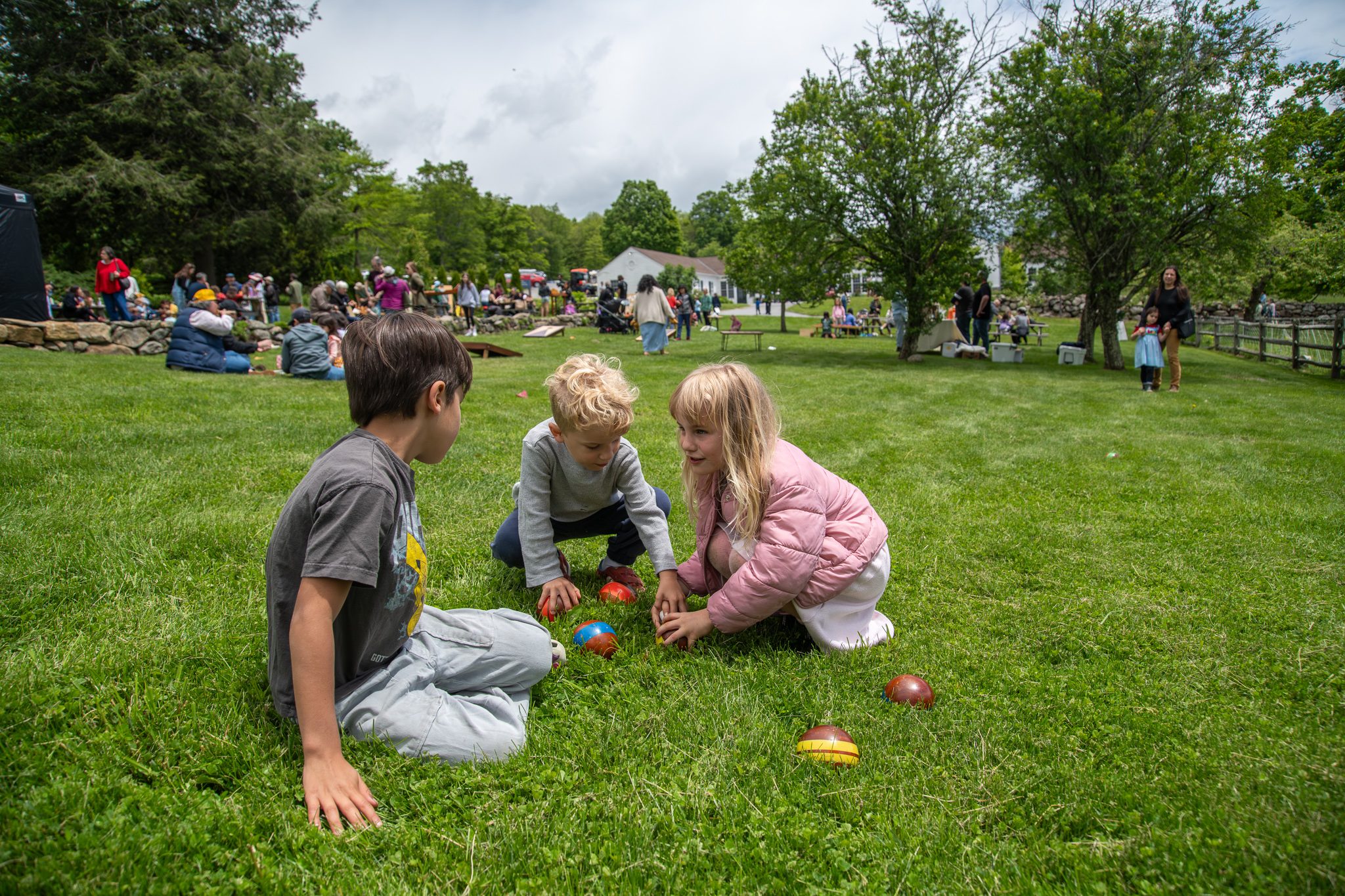 Three kids huddle over the bocce balls to see whose is closest.